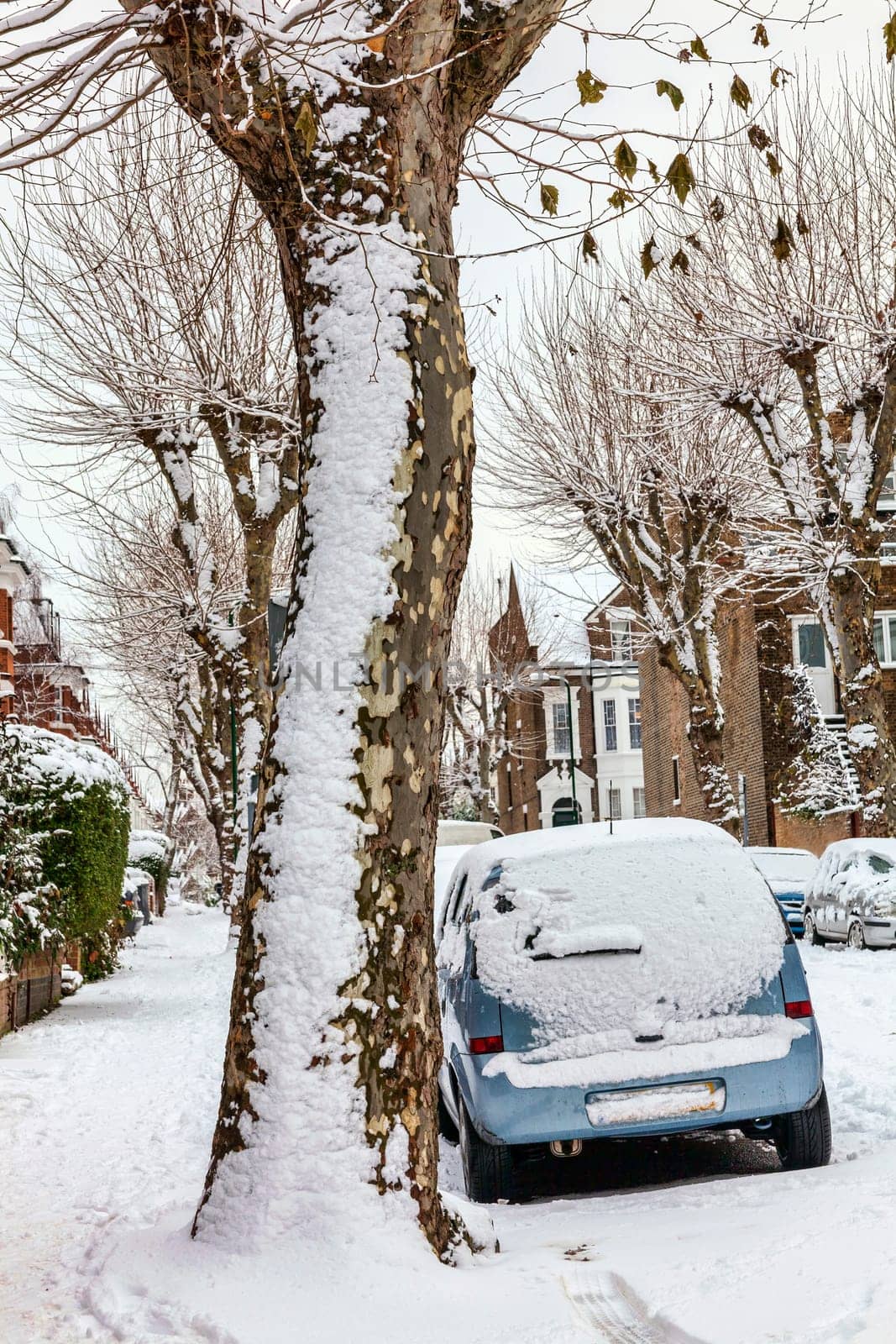 Street winter cityscape with snow terraced houses and frozen cars after a blizzard snowfall in London England UK, stock photo image with copy space