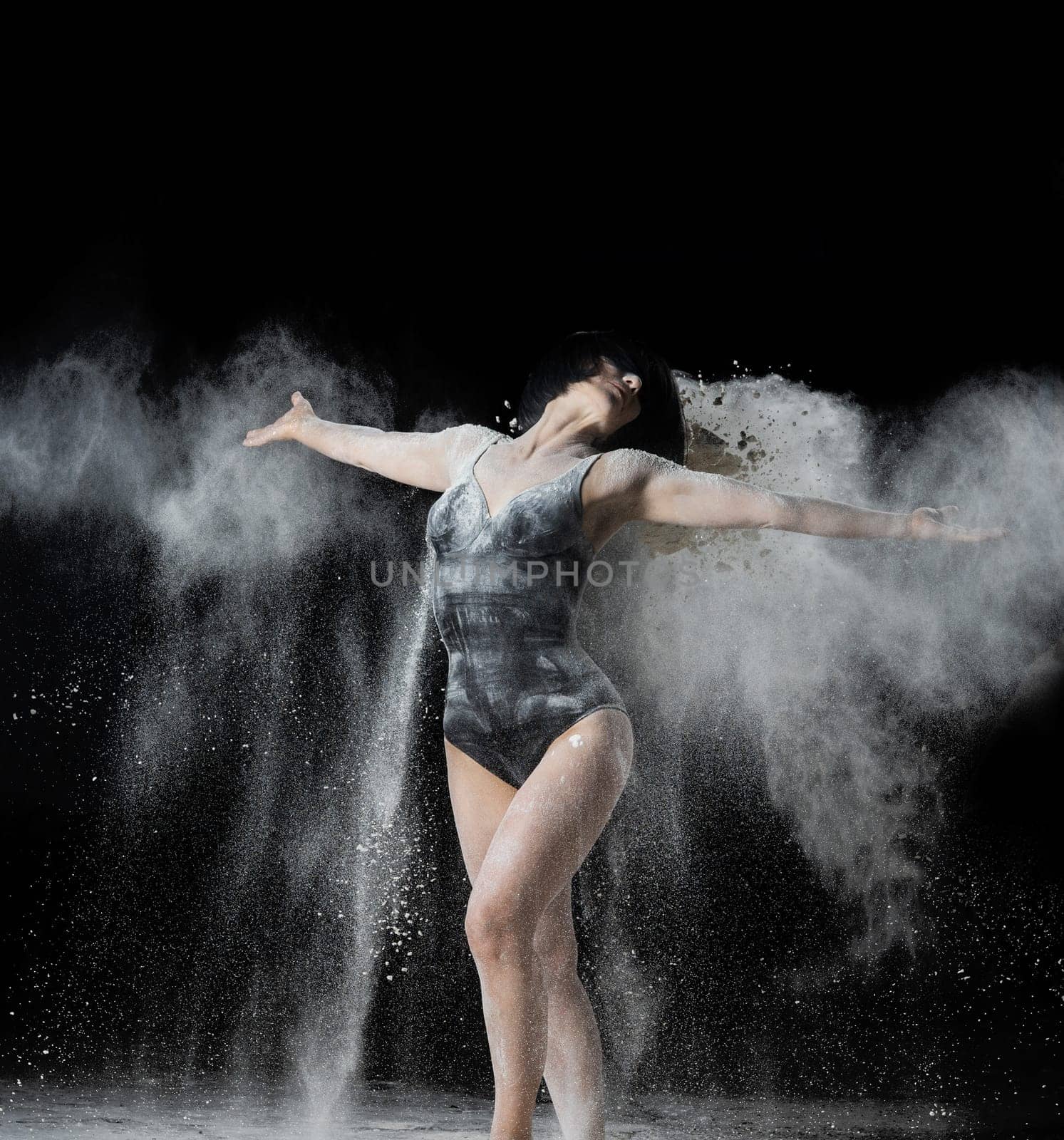 beautiful Caucasian woman throws white flour with her hands in different directions on a black background, graceful dance