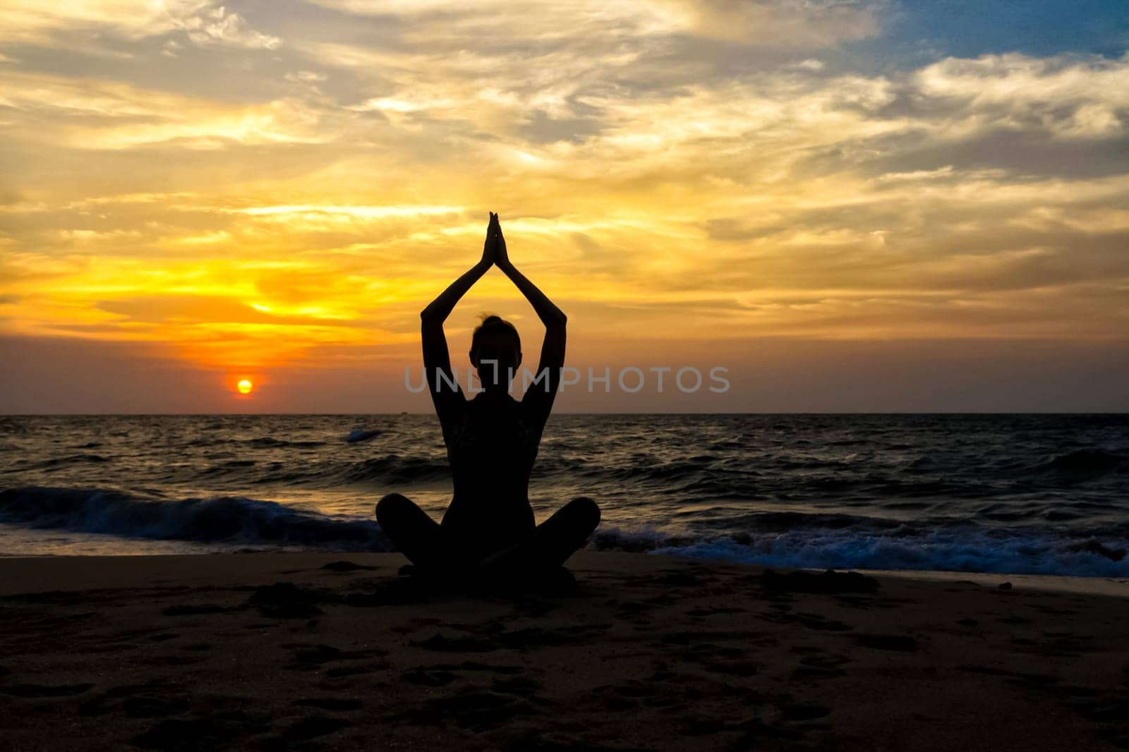 The figure of a girl on the background of the sea and sunset in a yoga pose on one leg.