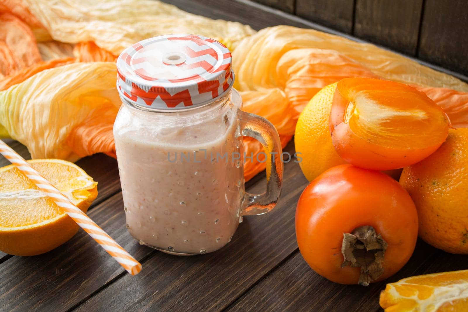 Fresh bright yellow smoothie with persimmon and orange on black wooden background