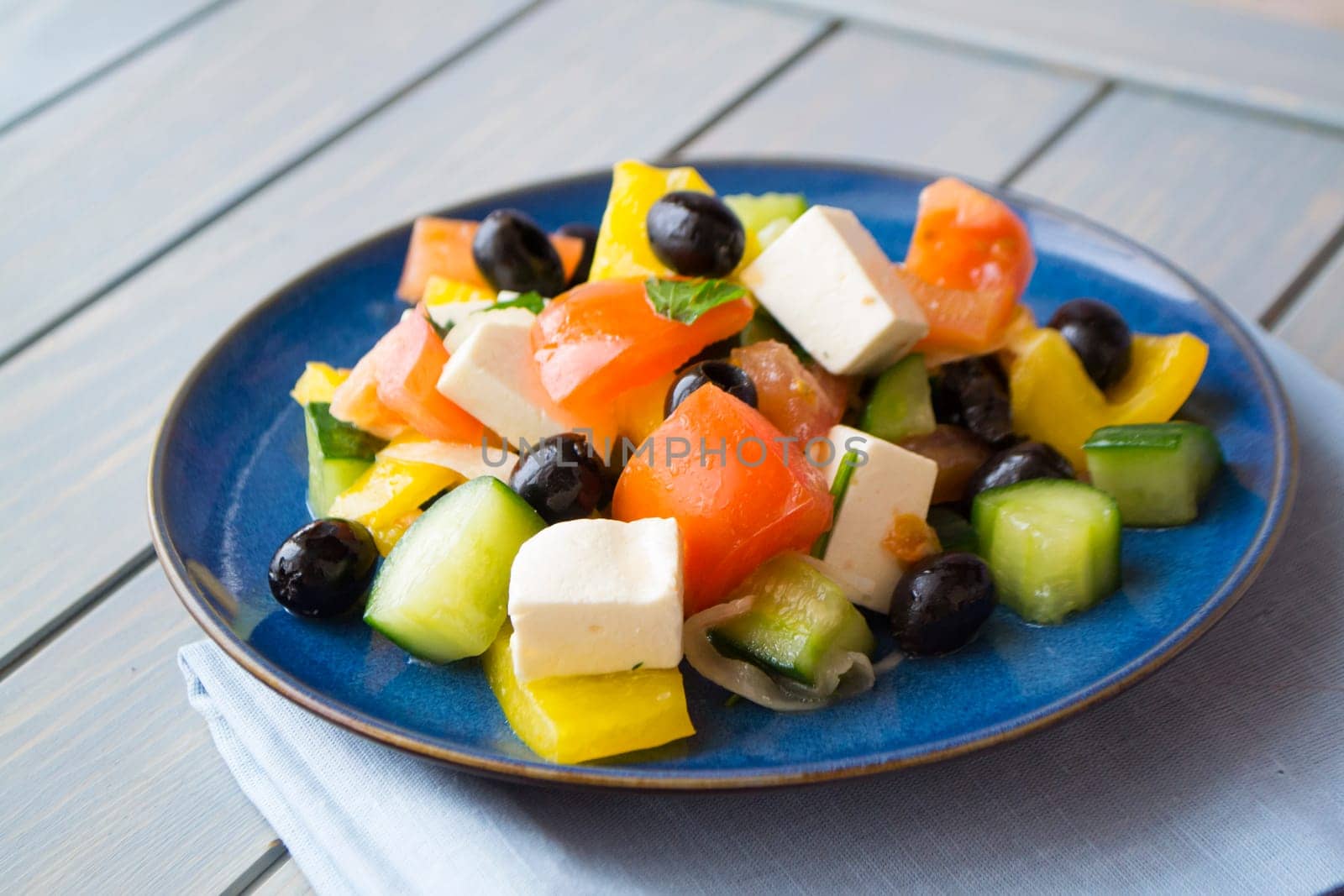 Greek salad with cucumber, tomato and pepper, lettuce, onion, feta cheese and olives on blue plate