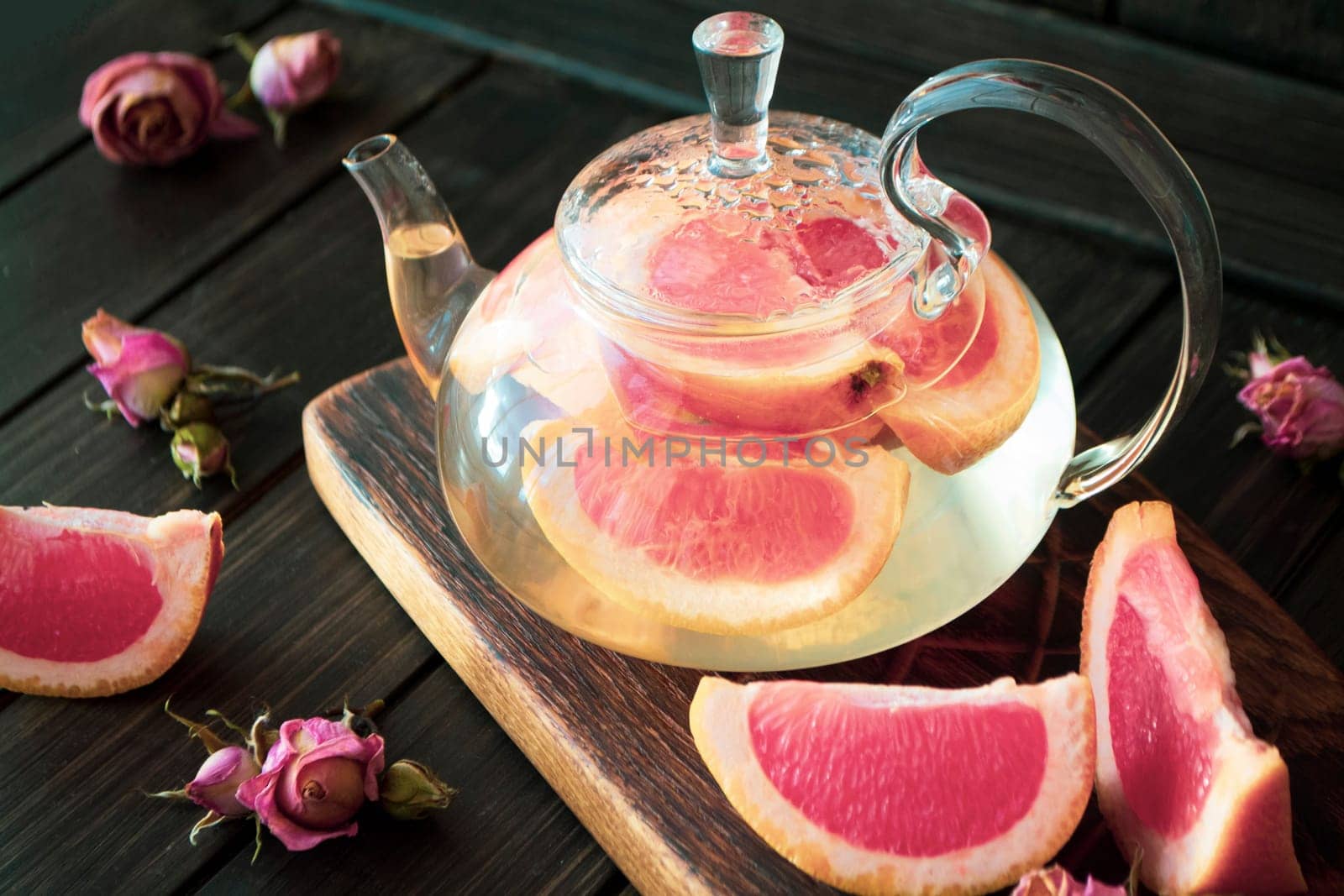 Pink grapefruit herbal tea with ginger and honey in a glass teapot on dark background