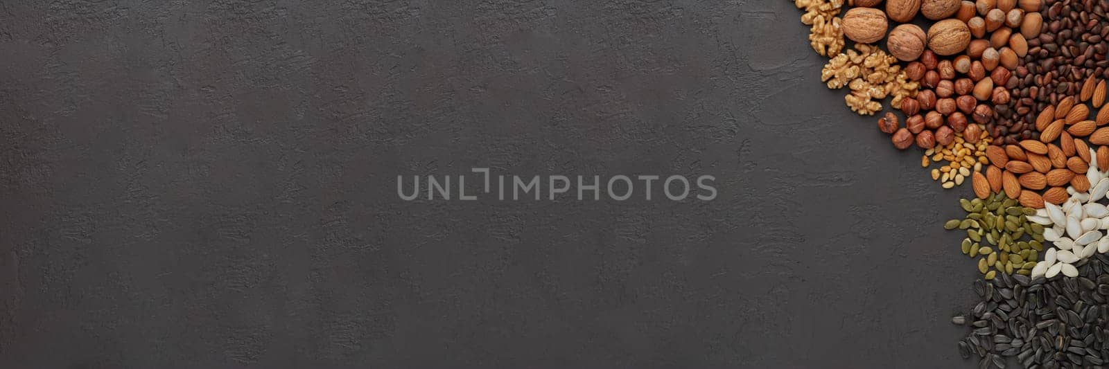 Different kinds nuts. Various varieties of nuts and seeds lying on black slate background. Top view with copy space. Healthy food. Vegetarian nutrition