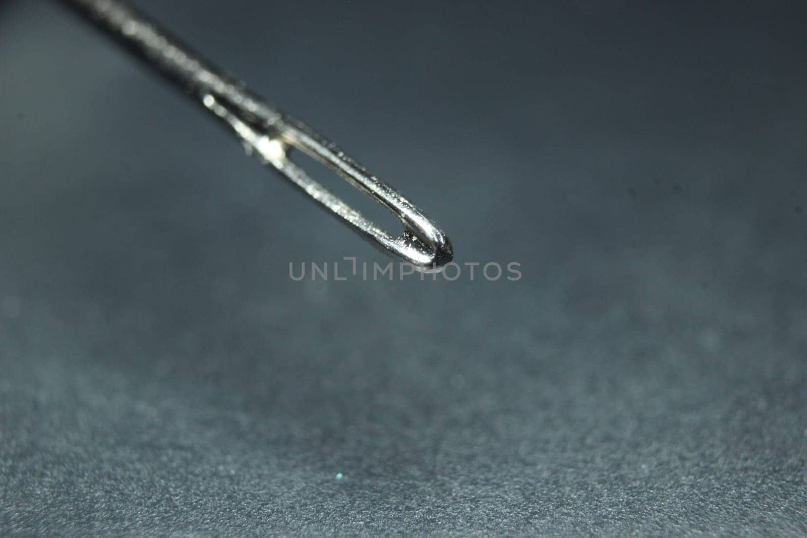 Macro photograph of sewing needle. Small needle with empty eyelet, isolated over the black background.