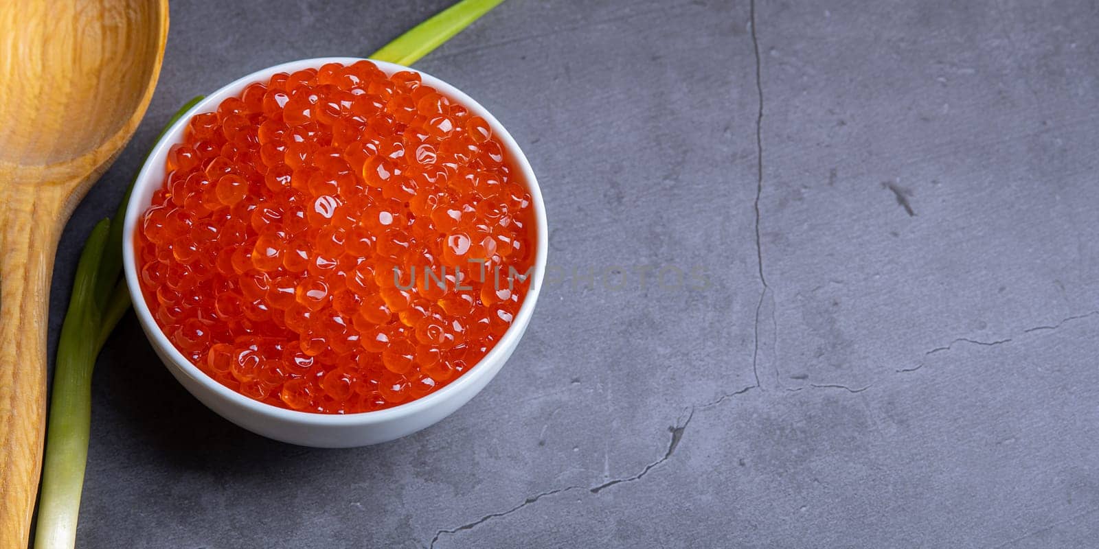 Red caviar in a wooden cup on a grey background with a spoon. Place for advertisement, logo, label, mockup, mock-up.