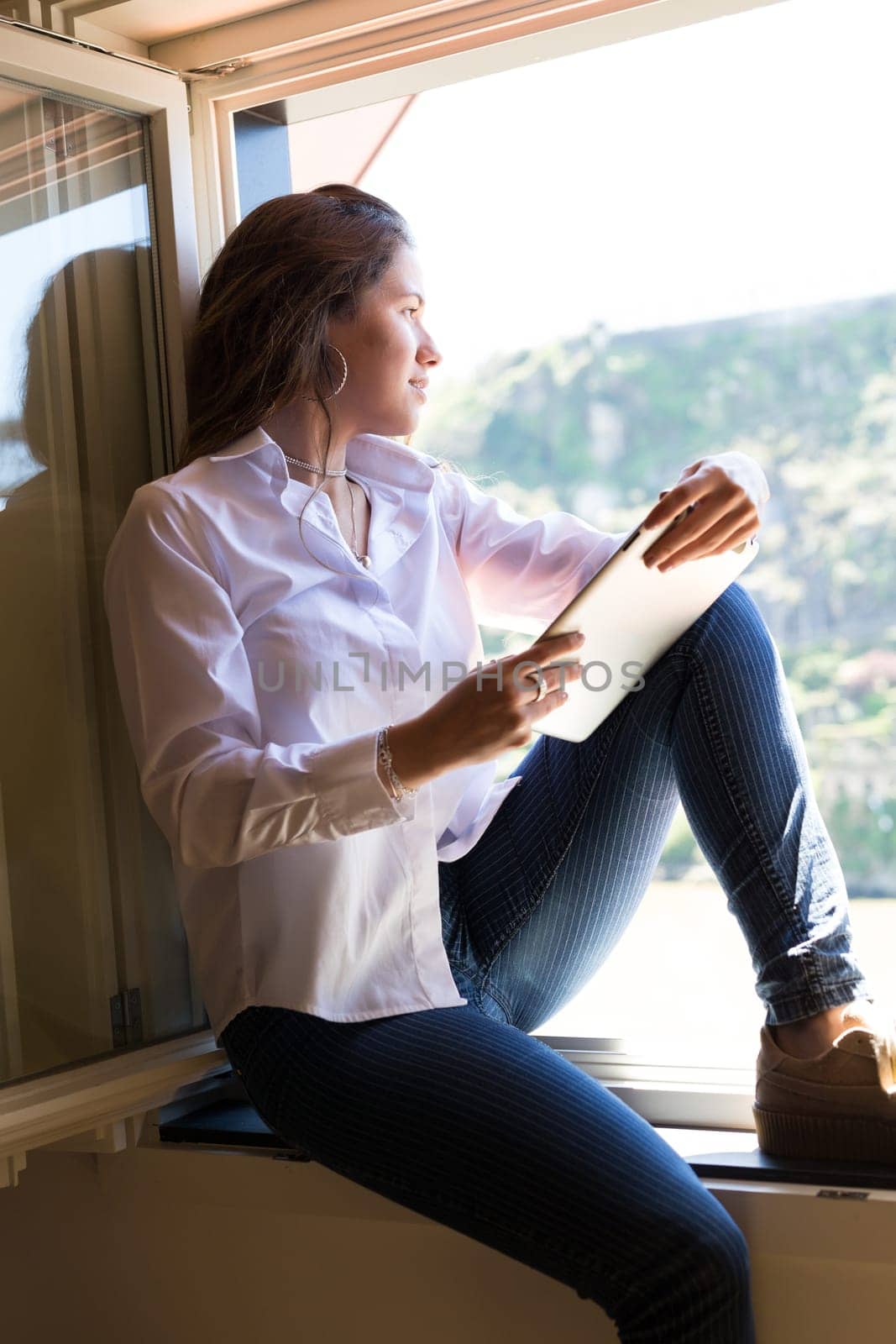 Young woman catching some sun at the balcony and checking the social networks