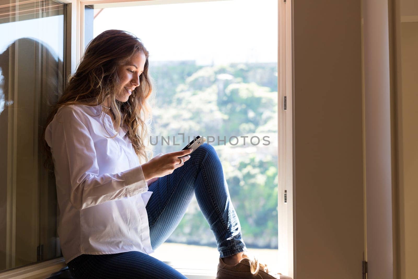 Young woman catching some sun at the balcony while using her new smartphone