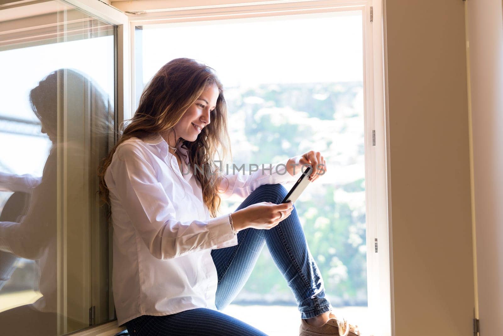 Young woman catching some sun at the balcony while using her new smartphone