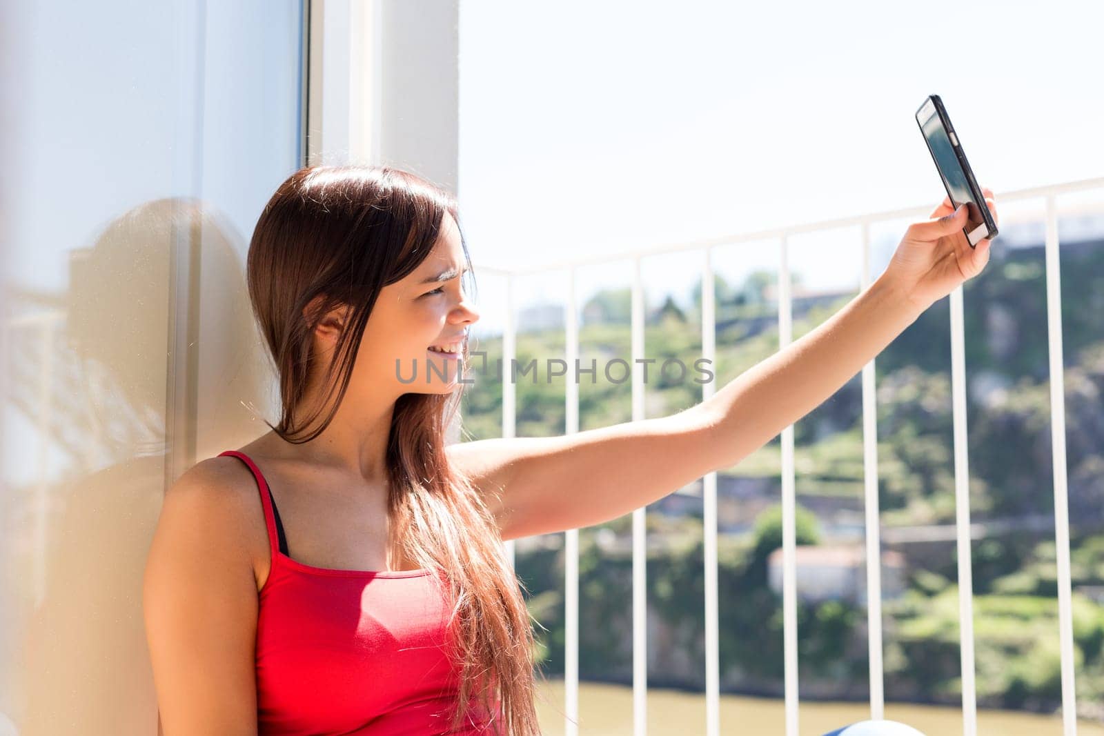Young woman catching some sun at the balcony while using her new smartphone