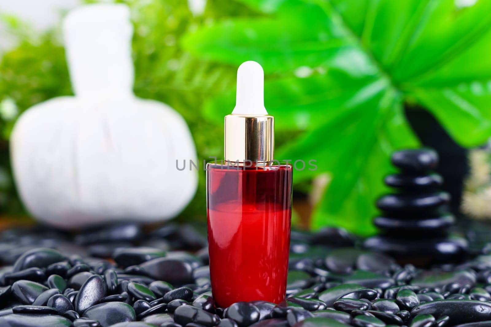 Thai Spa massage setting with red serum oil bottle dropper mock up or essential oil on black stone