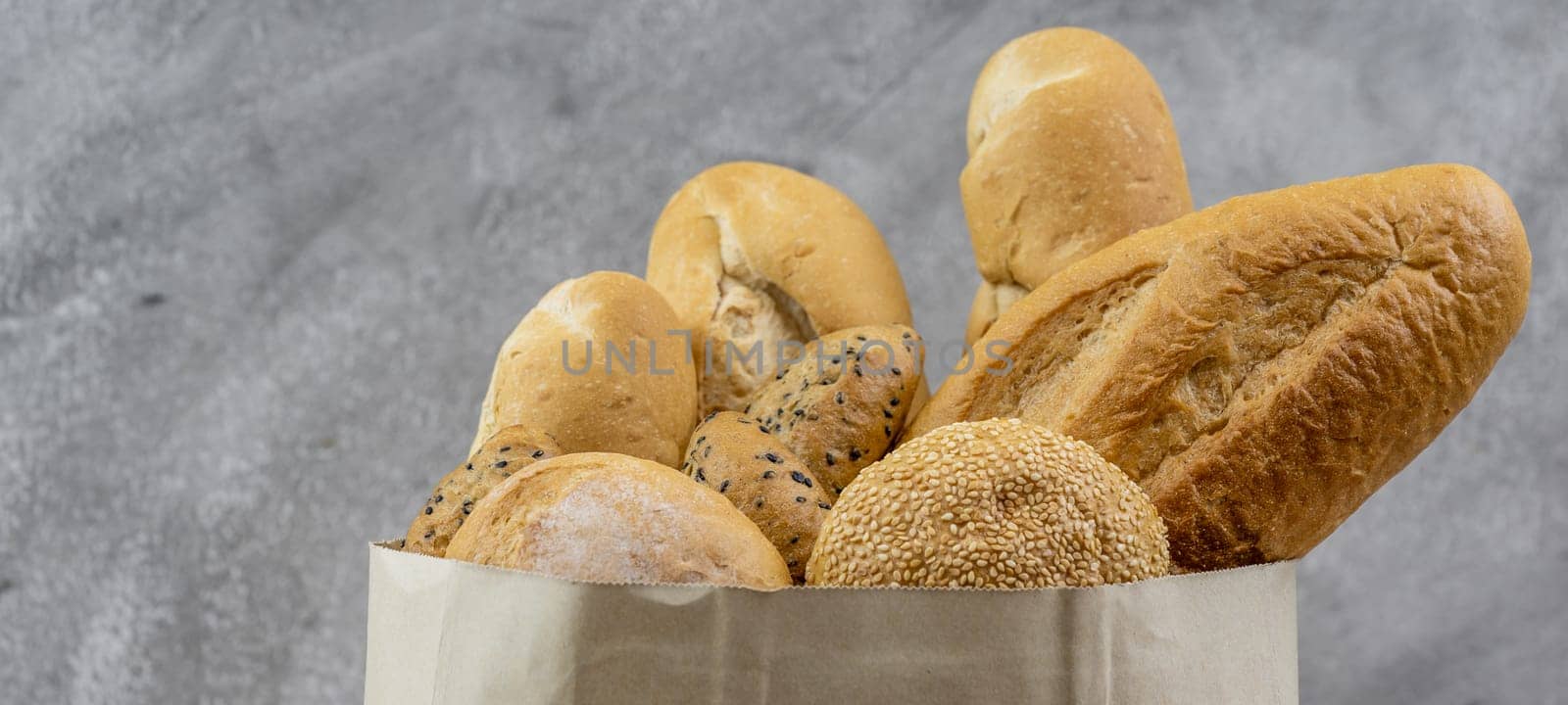 Variety bread in disposable paper bag on grey vintage loft background. Bakery food and drink and grocery concept for delivery. Panoramic web banner crop.
