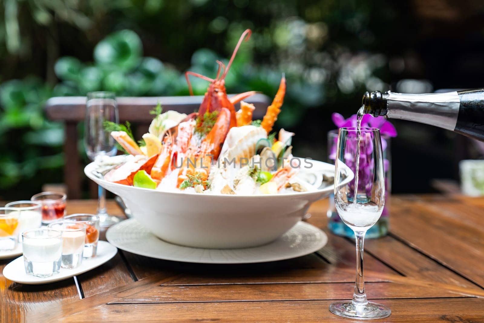 Waiter pouring white wine into wine glass and serving to customer in restaurant with big bowl seafood on ice in background. Restaurant gastronomy food and drink consumerism concept.