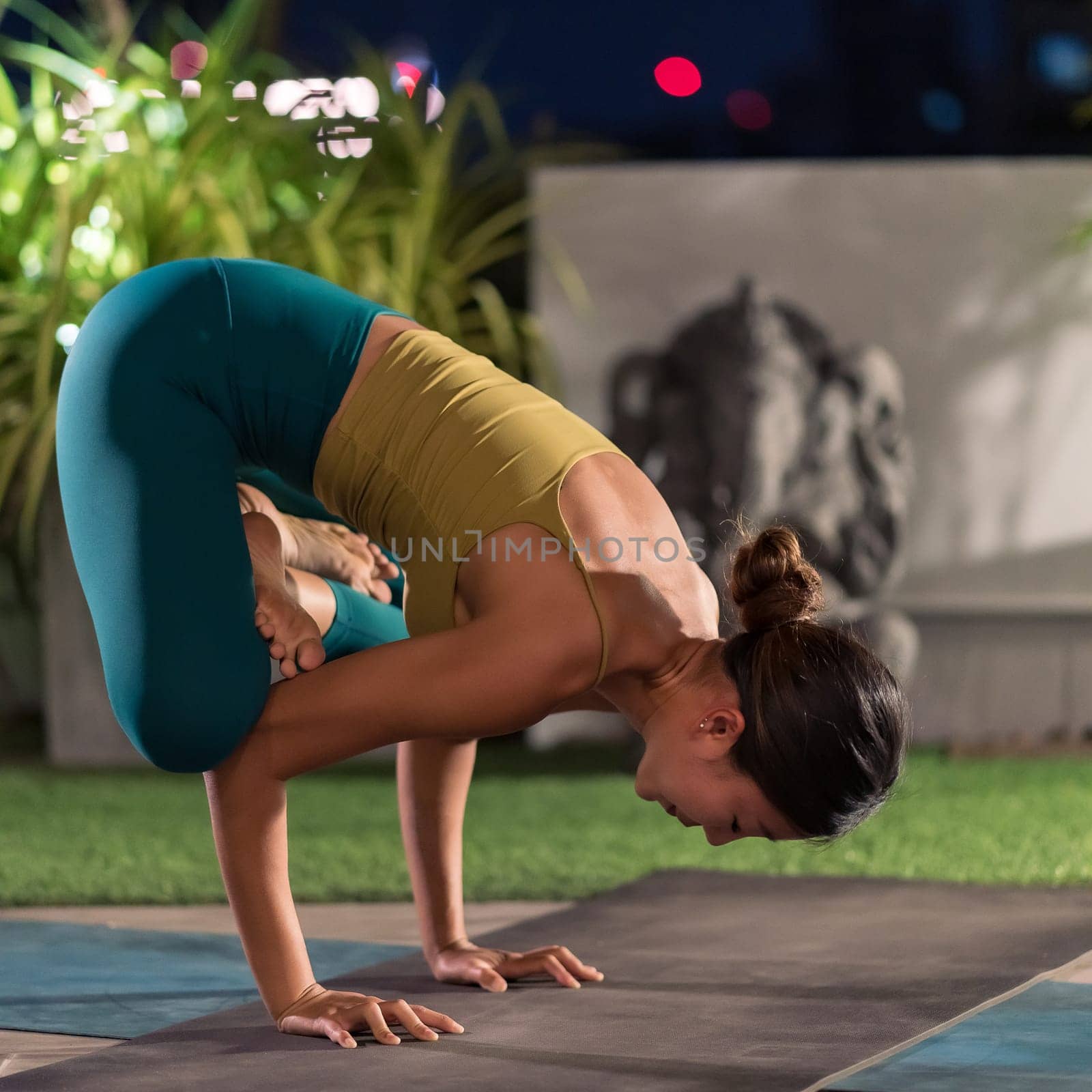 Asian female woman in sportswear bra pants practicing yoga during city lockdown alone in her apratment with background of cityscape illumination at night. Work out fitness healthy lifestyle concept.