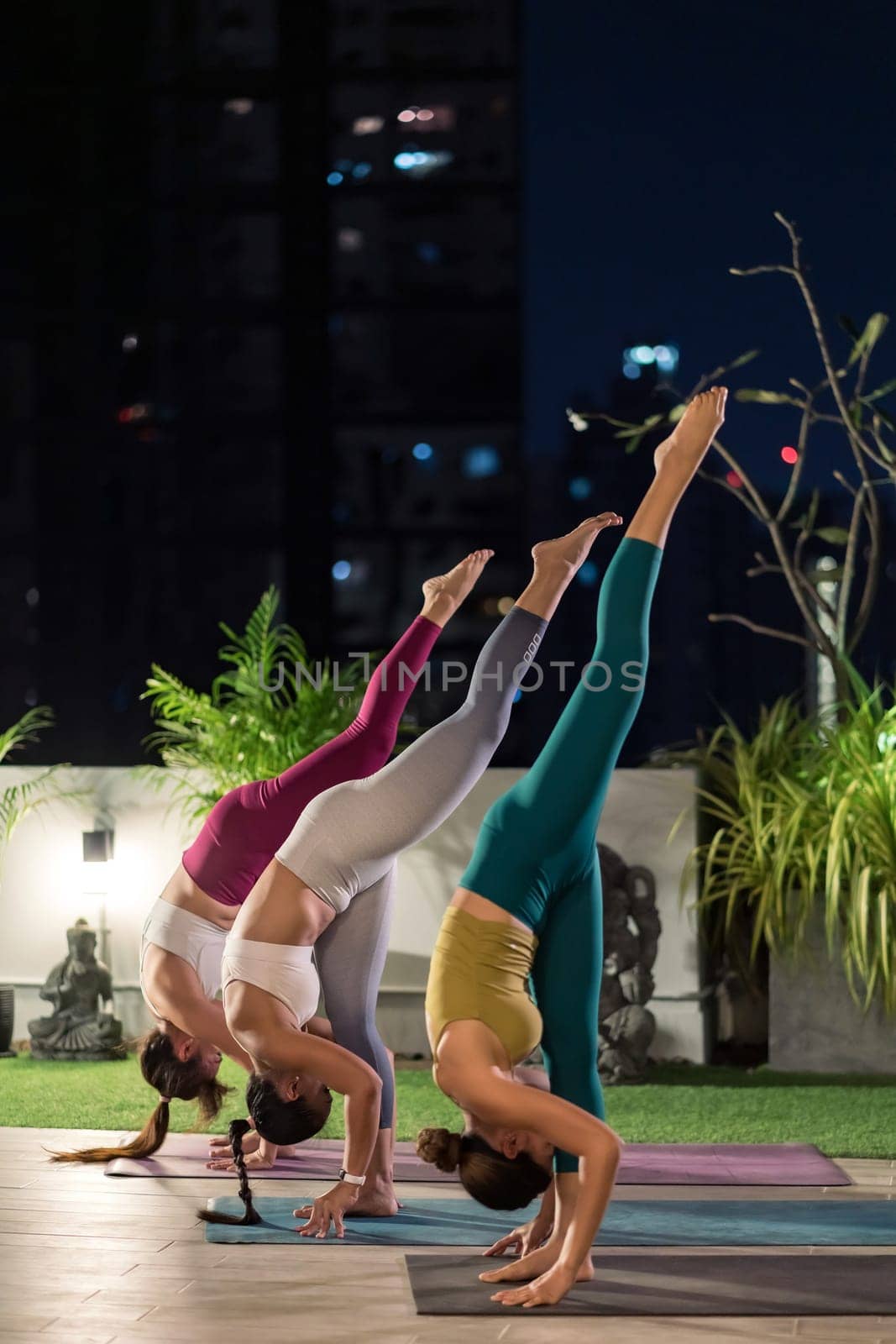 Group of asian women in sportswear pants practicing yoga during city lockdown in their apratment with distance in background of cityscape illumination night. Work out fitness healthy lifestyle concept