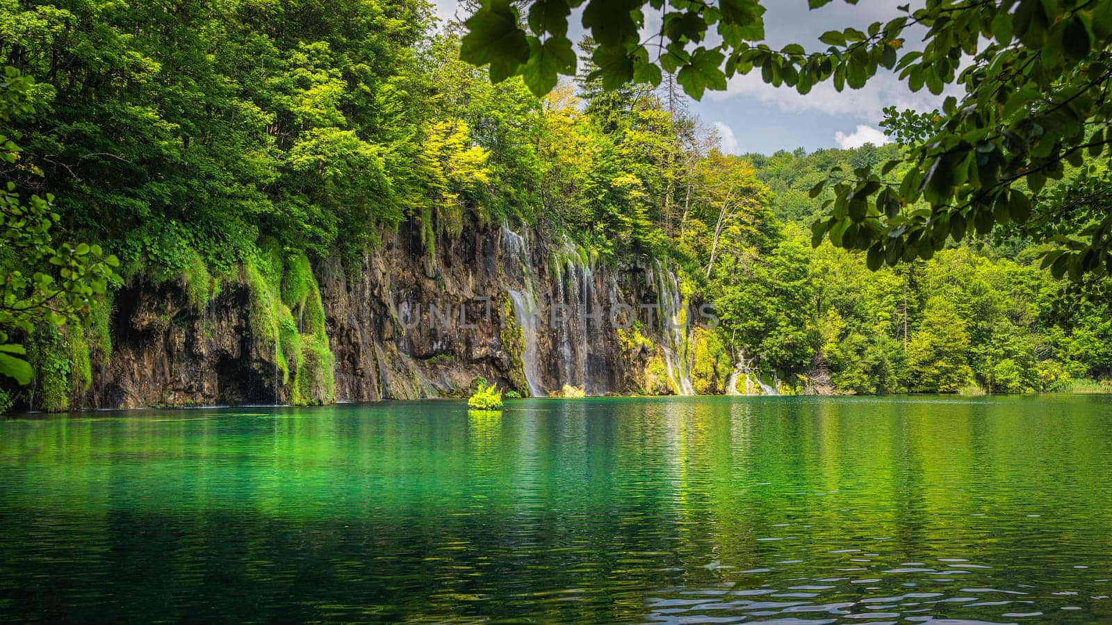 Beautiful waterfall illuminated by sunlight with reflections in lake. Green lush forest, Plitvice Lakes National Park UNESCO World Heritage in Croatia