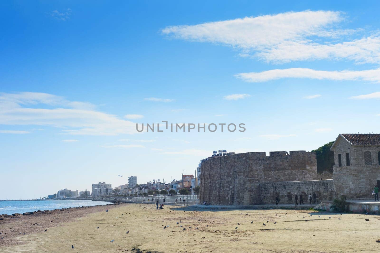 LARNACA, CYPRUS - FEBRUARY 17, 2019: People walking at the resort embankment of Larnaca, Laranaca Castle and fort in the background