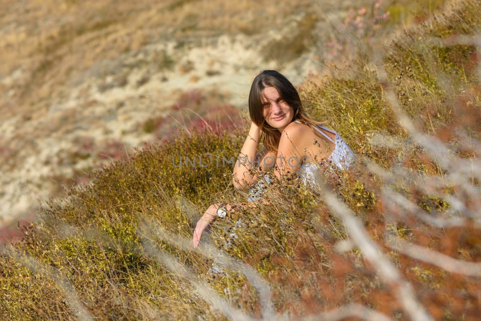 A girl sits in a field, against a background of blurred wildflowers on a sunny day