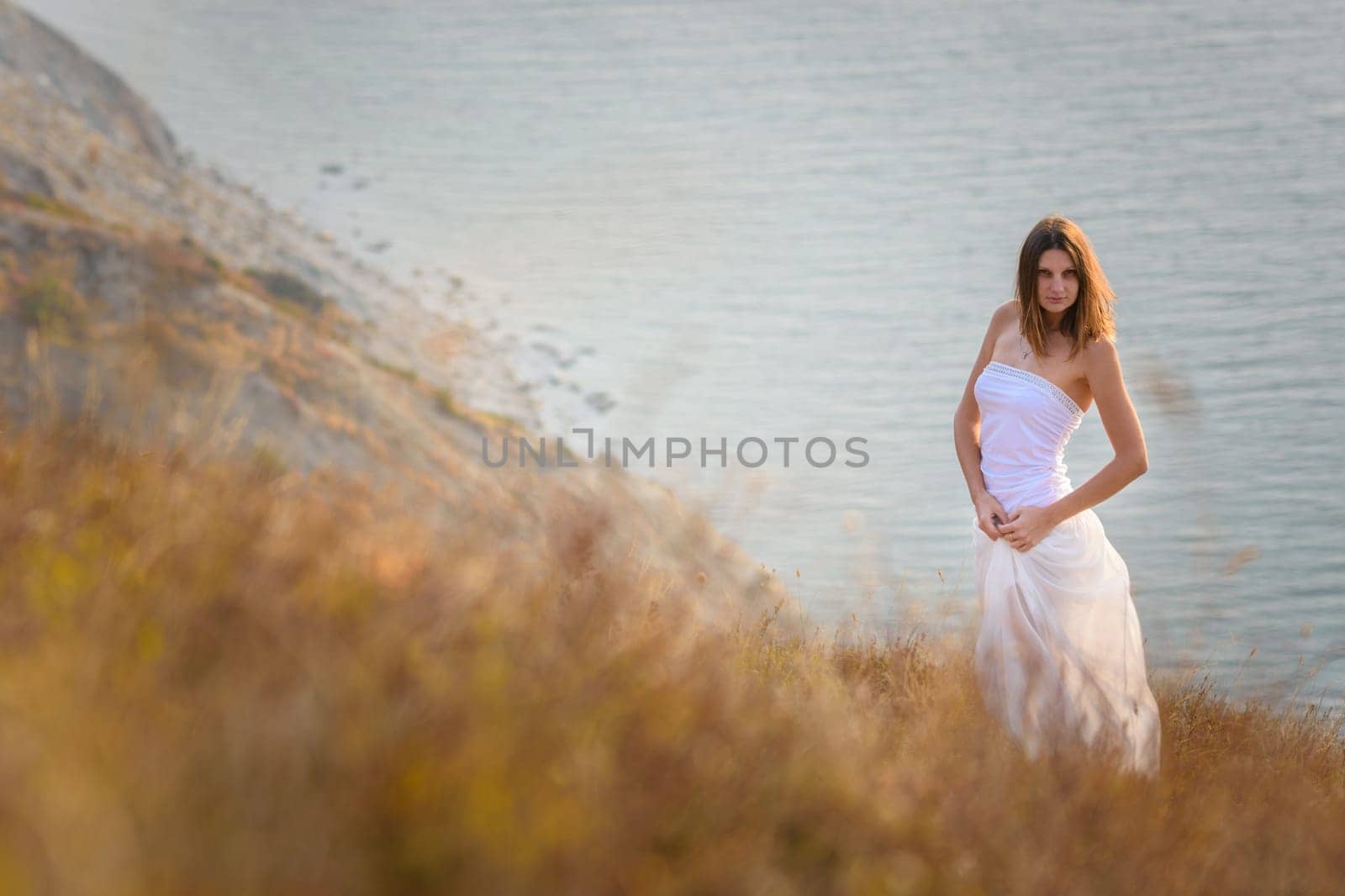 A beautiful slender girl stands on a hillock against the background of the sea