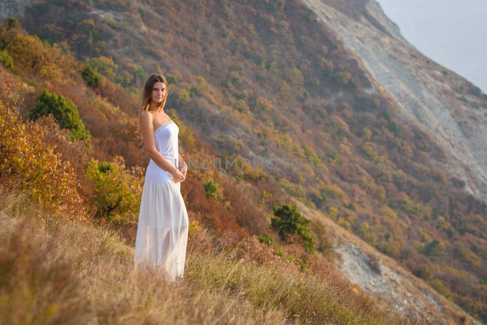 A beautiful girl stands on a hill by the sea