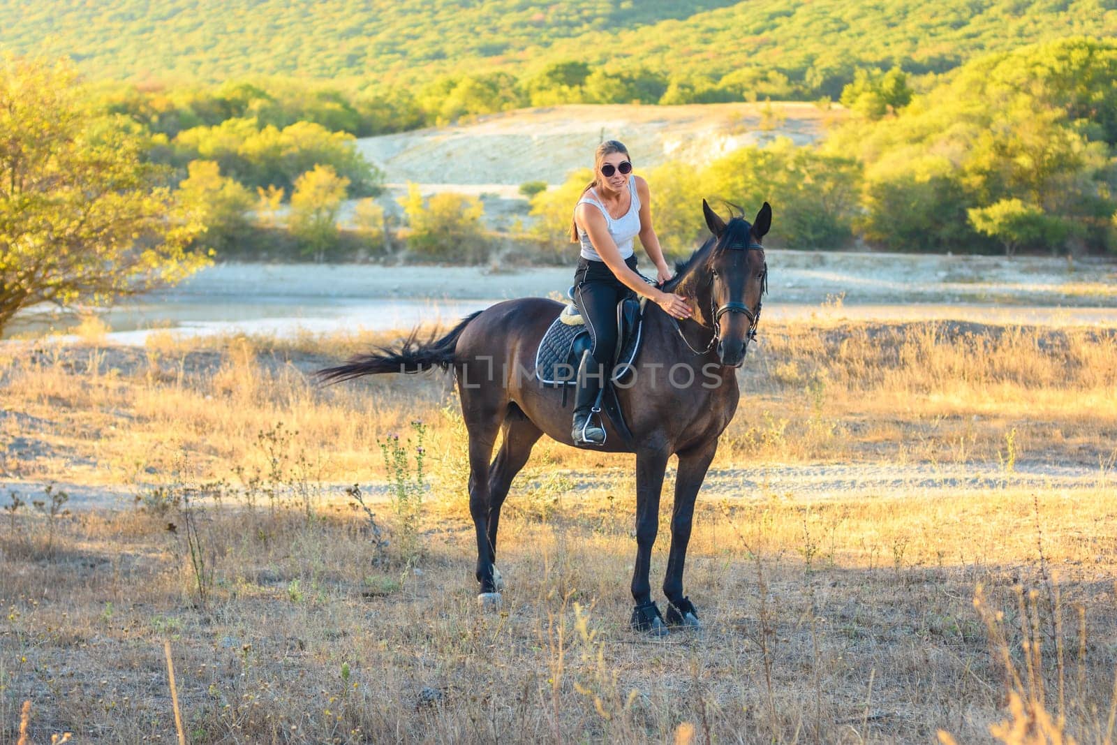 Girl with glasses strokes a horse riding in the autumn forest