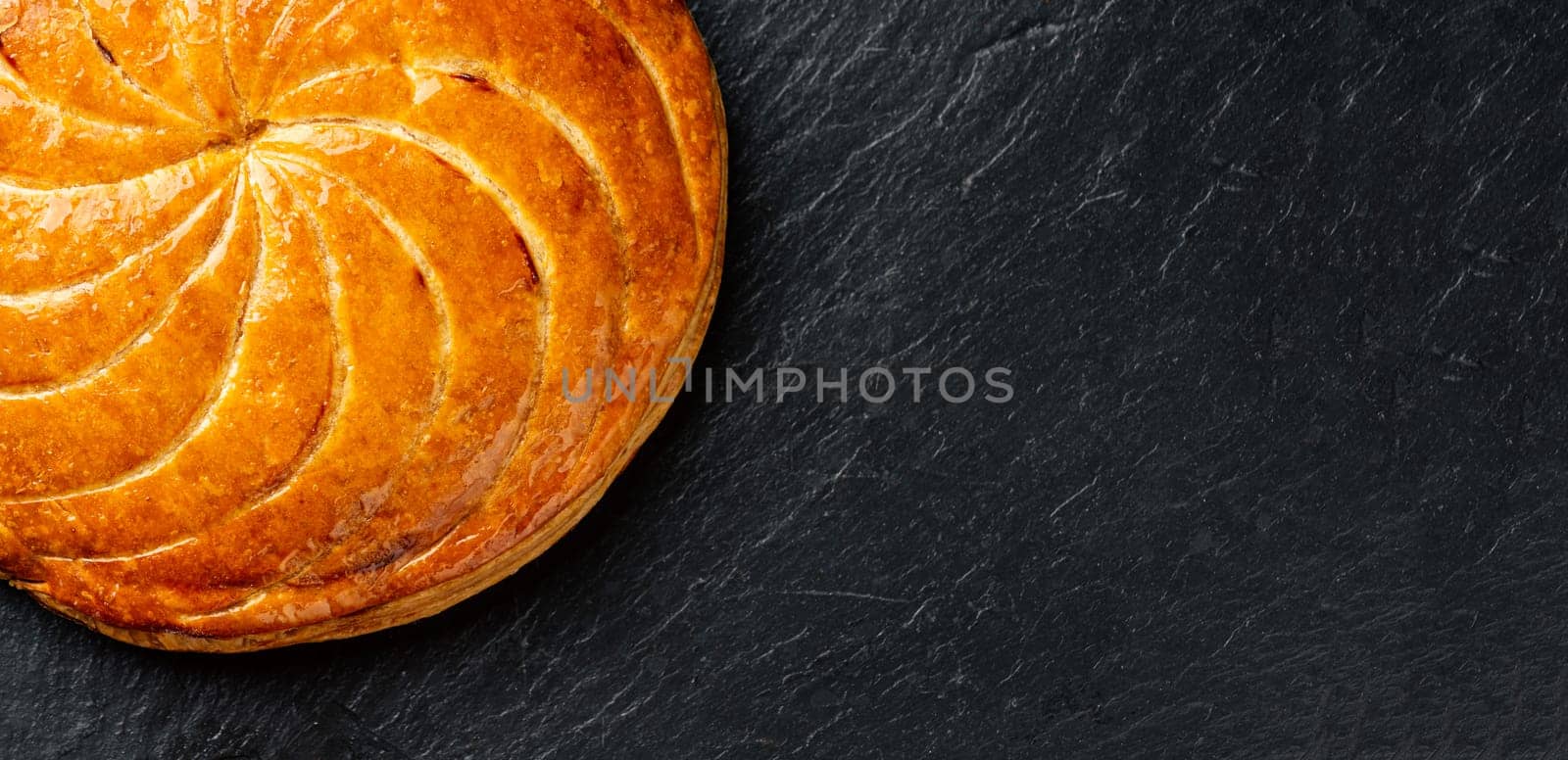Epiphany cake or galette des rois in French on black slate background, panoramic crop with copy space
