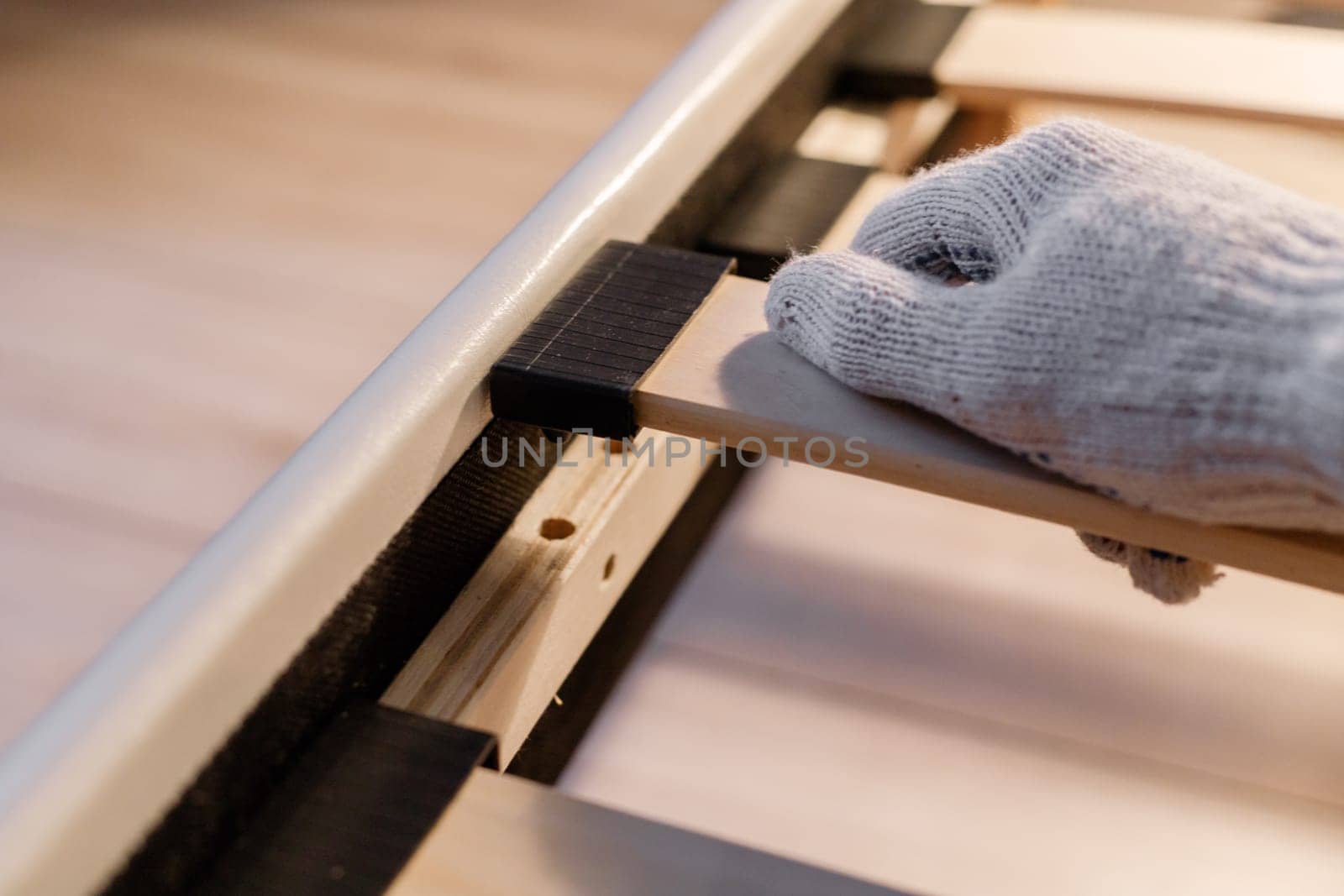 Male worker's hand in glove assembling bed, connecting slats to bed frame.