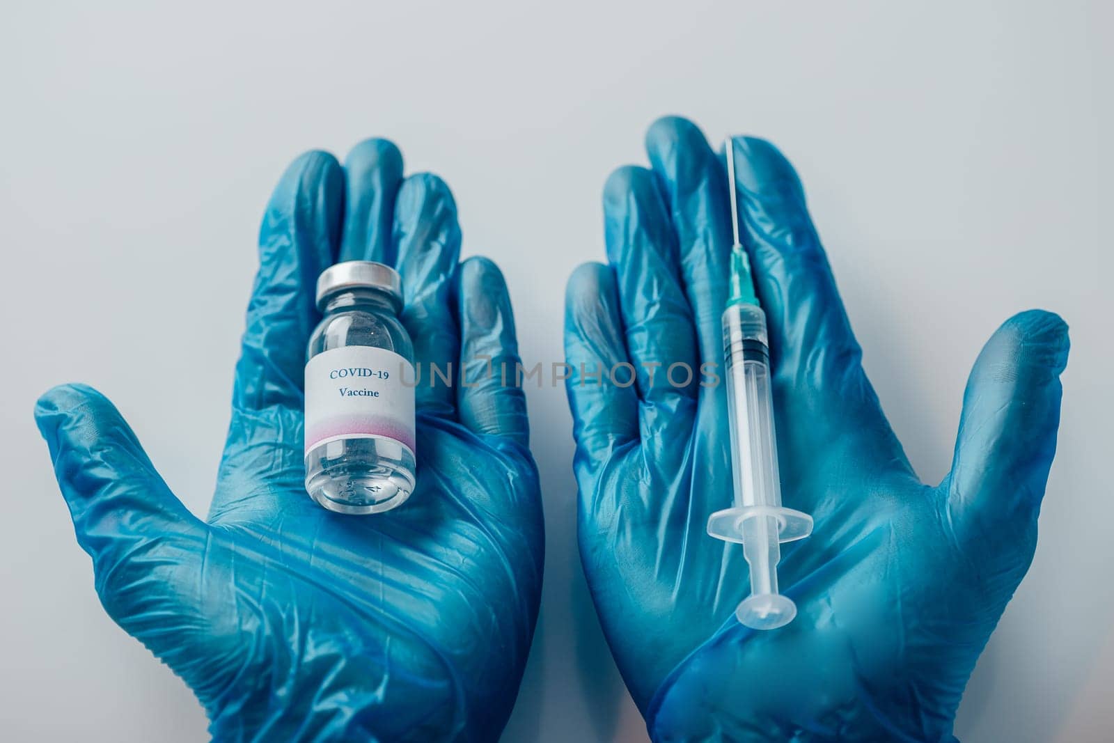 Top view of a hand in blue medical gloves holding a medical syringe and vial with COVID-19 vaccine. Concept of immunization and biotechnological development.