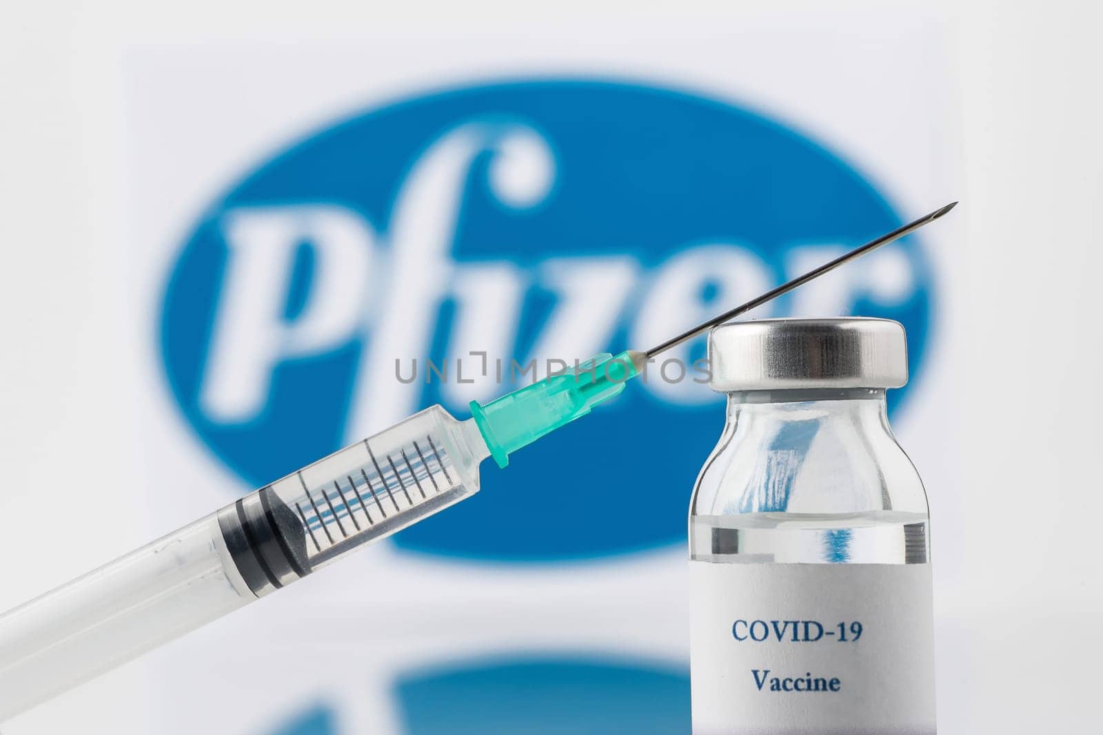 Teo, Spain  December 21 2020: Pfizer Covid-19 vaccine concept Close-up of a syringe and a vial, the Pfizer company logo blurred in the background.