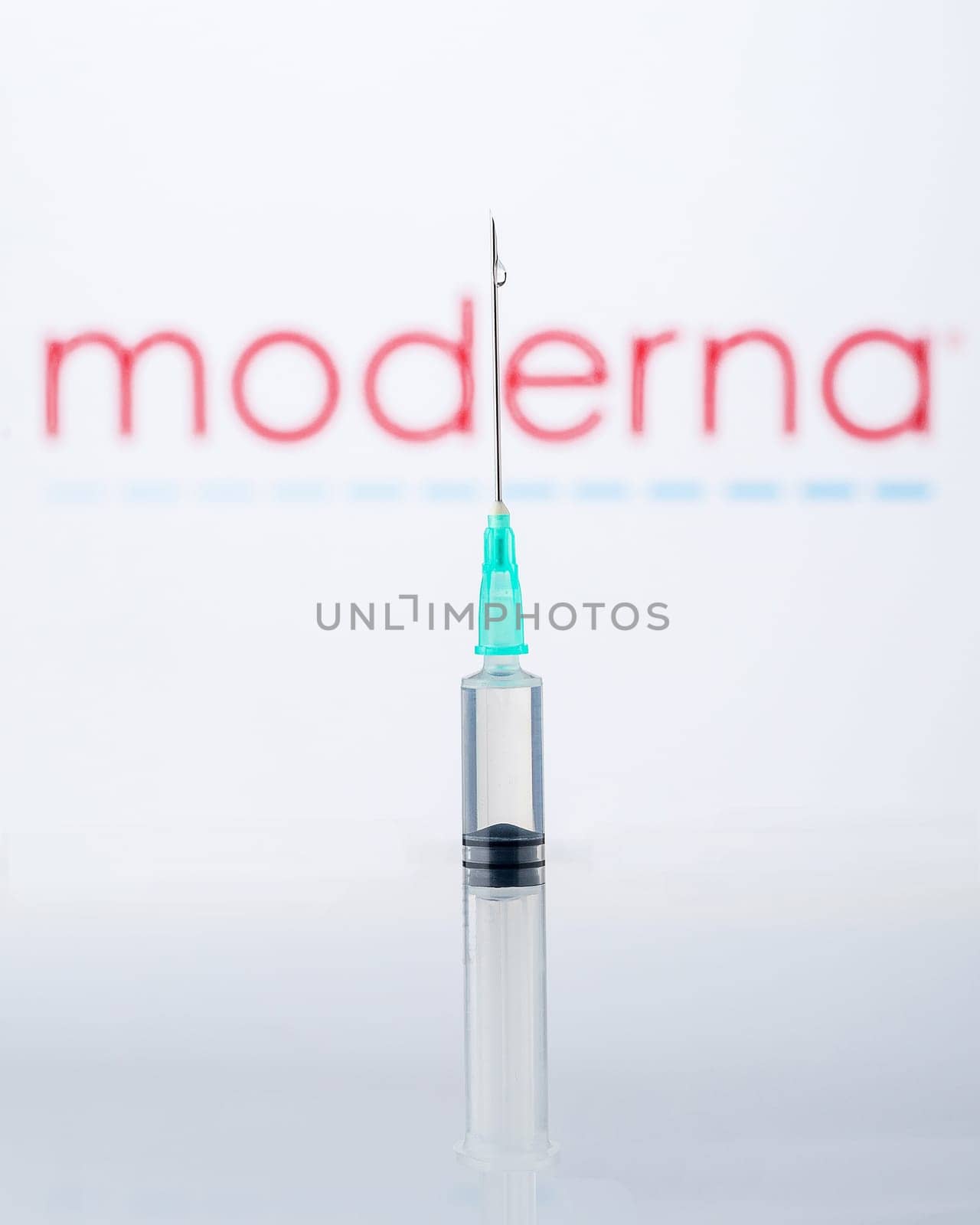 Teo, Spain  December 22 2020: Moderna Covid-19 vaccine concept. Close-up of a syringe and a drop of liquid on it, the Moderna company logo blurred in the background.
