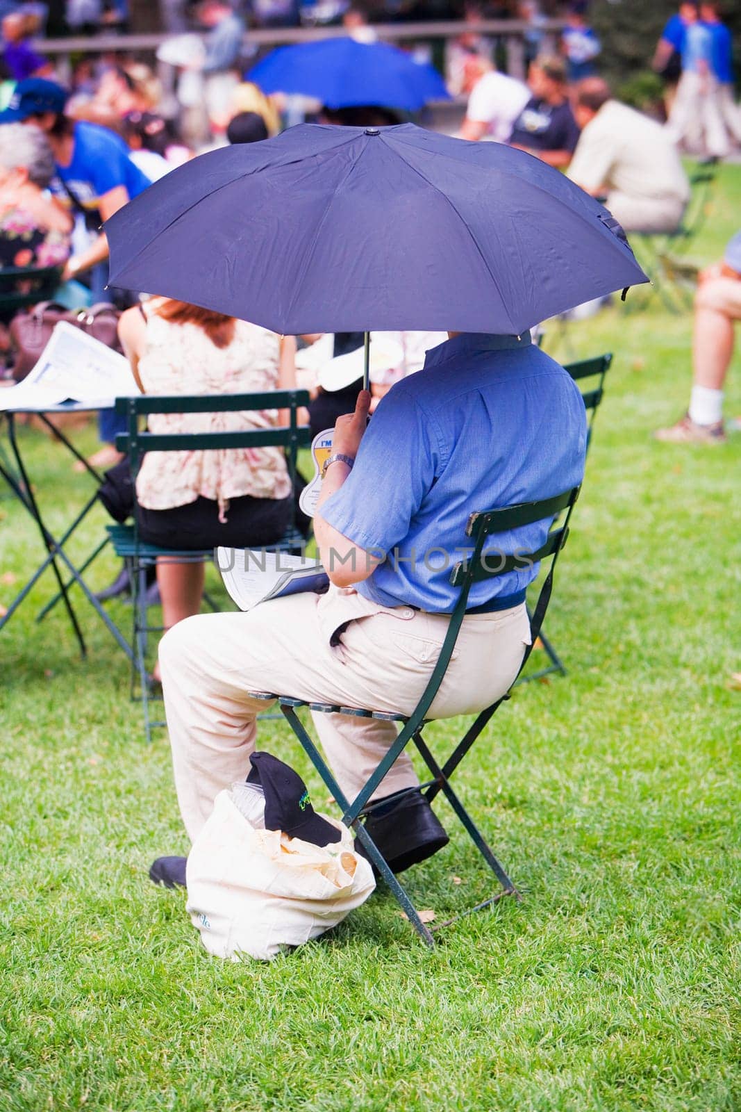 Rear view of a man sitting on a folding chair and holding an umbrella