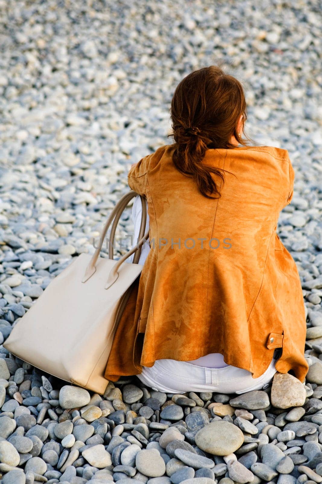 Rear view of a woman sitting on pebbles