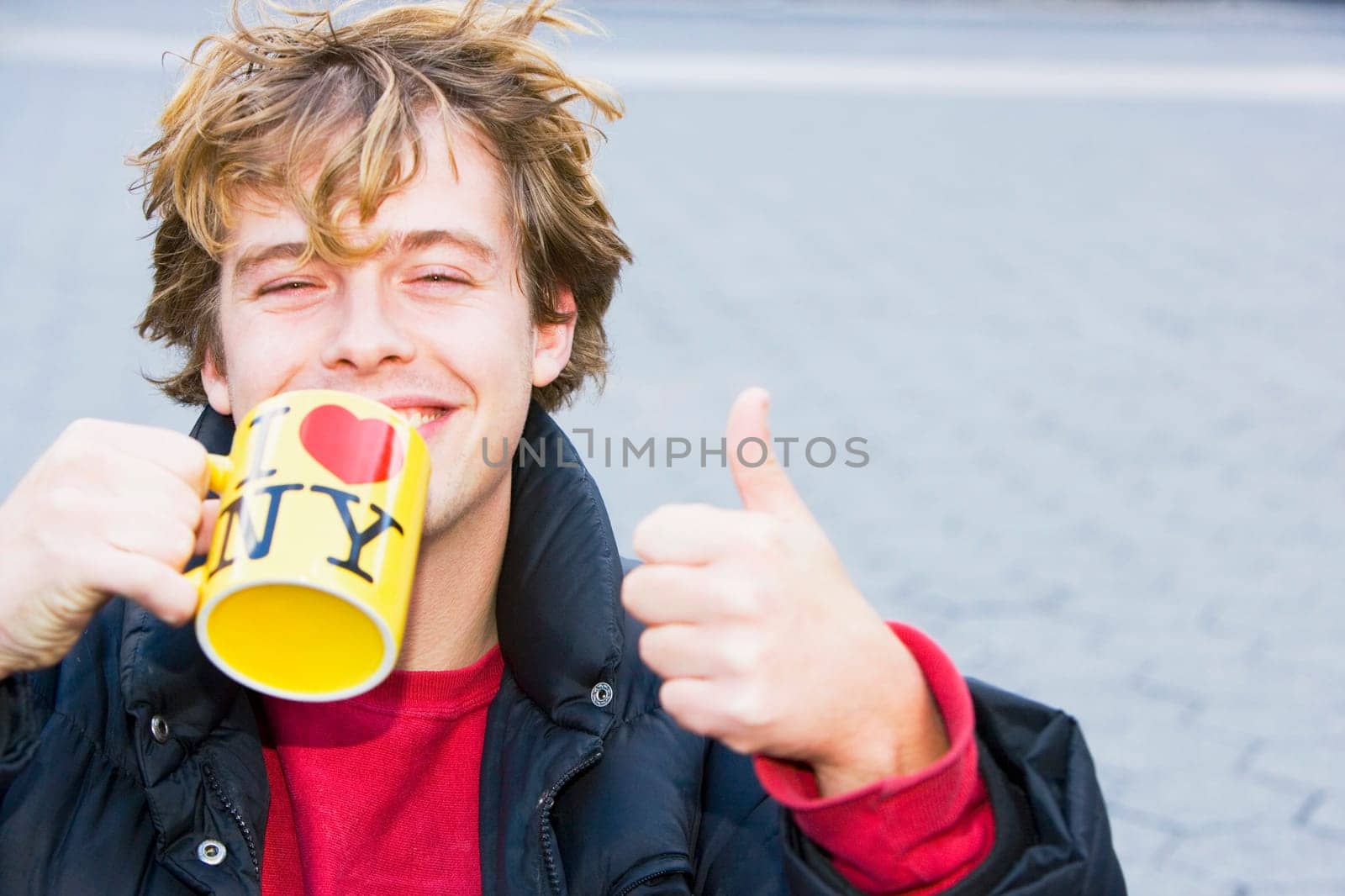 Portrait of a young man holding a coffee cup and showing a thumbs up sign