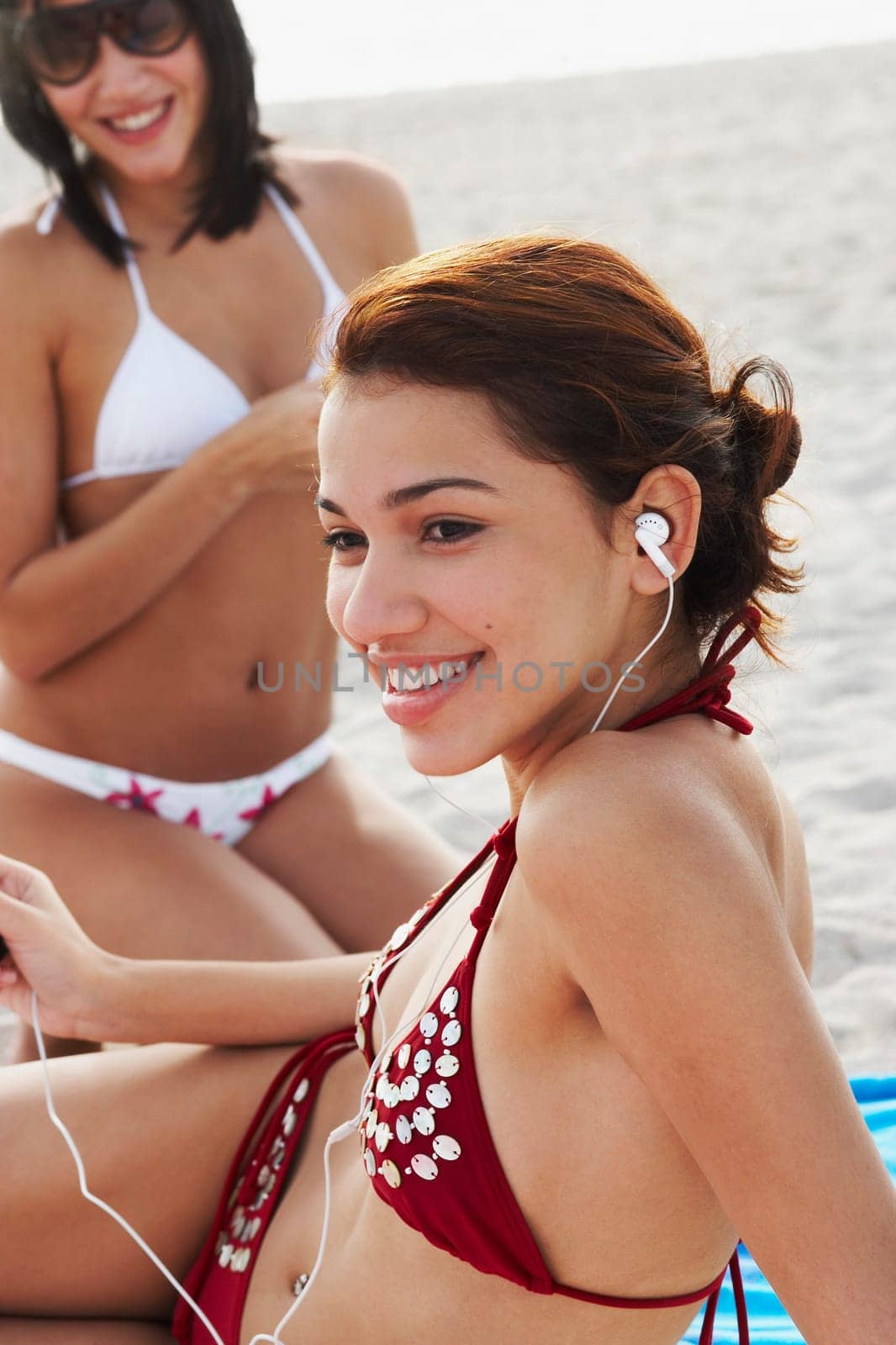 Young women listening to music and talking on cell phone while sunbathing on beach