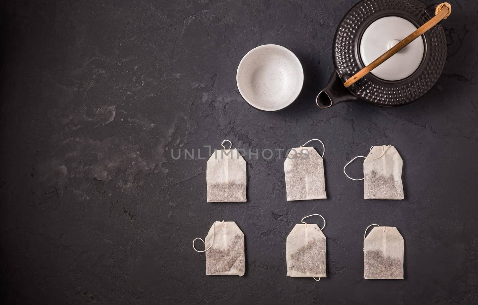 Assorted tea bags with tea pot and cup on black stone background