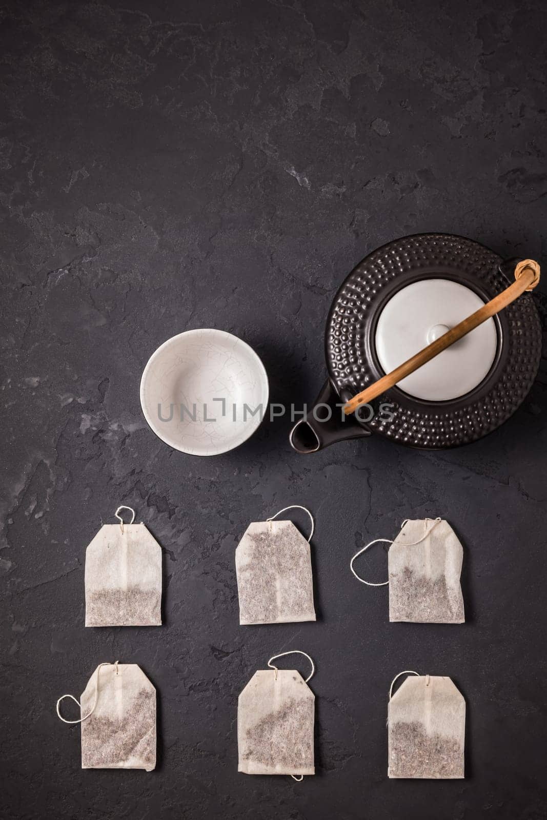 Assorted tea bags with tea pot and cup on black stone background