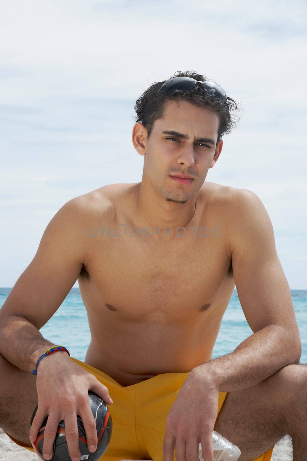 Portrait of a young man sitting on the beach and holding a soccer ball