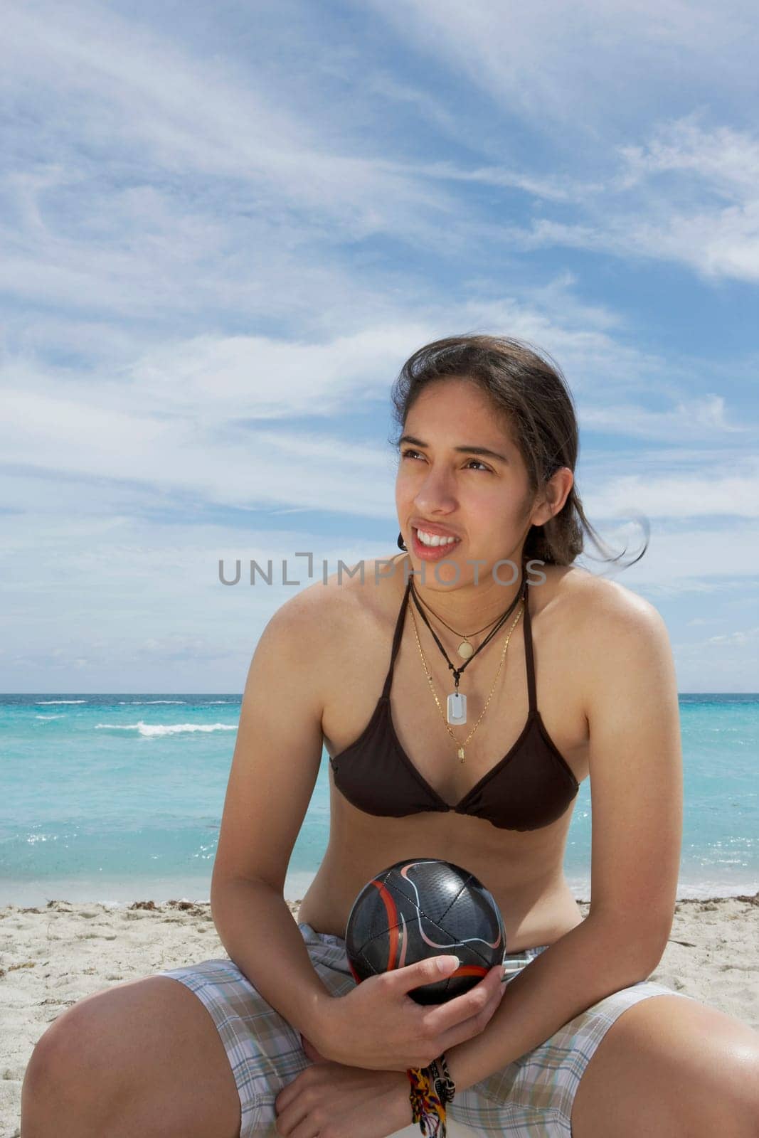 Young woman sitting on the beach and holding a soccer ball