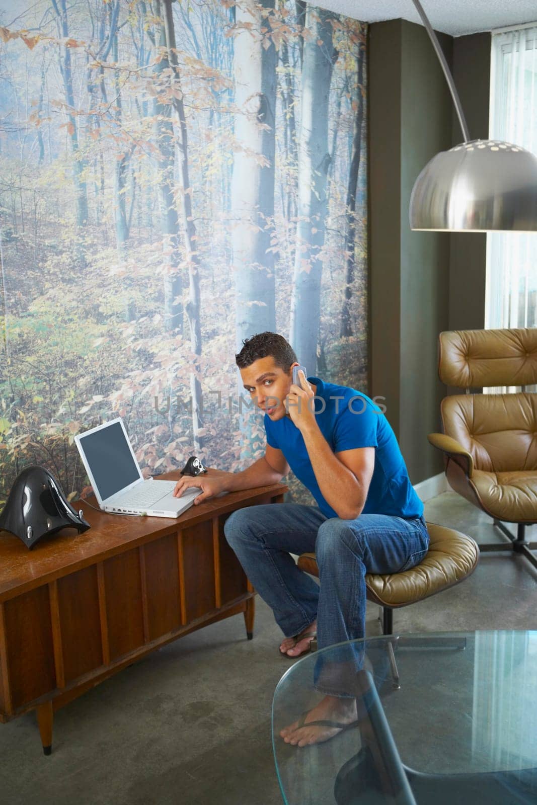 Portrait of a young man talking on a mobile phone while using a laptop