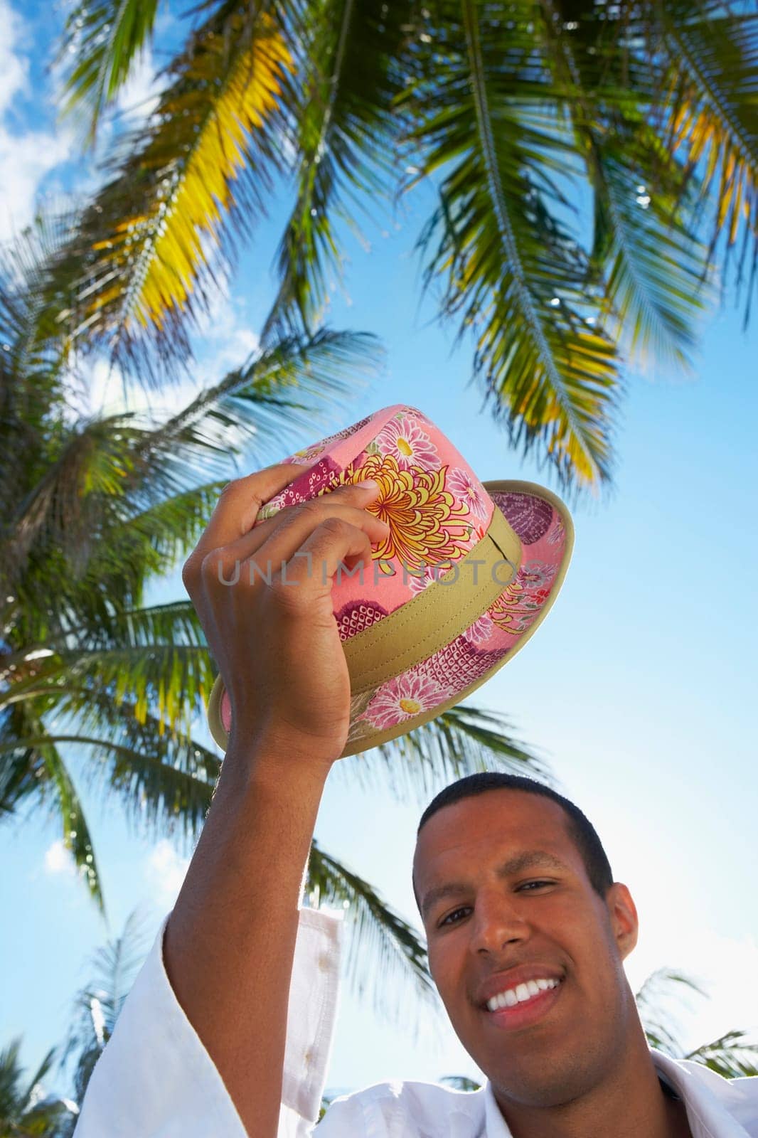 Portrait of a young man holding a hat above his head and smiling