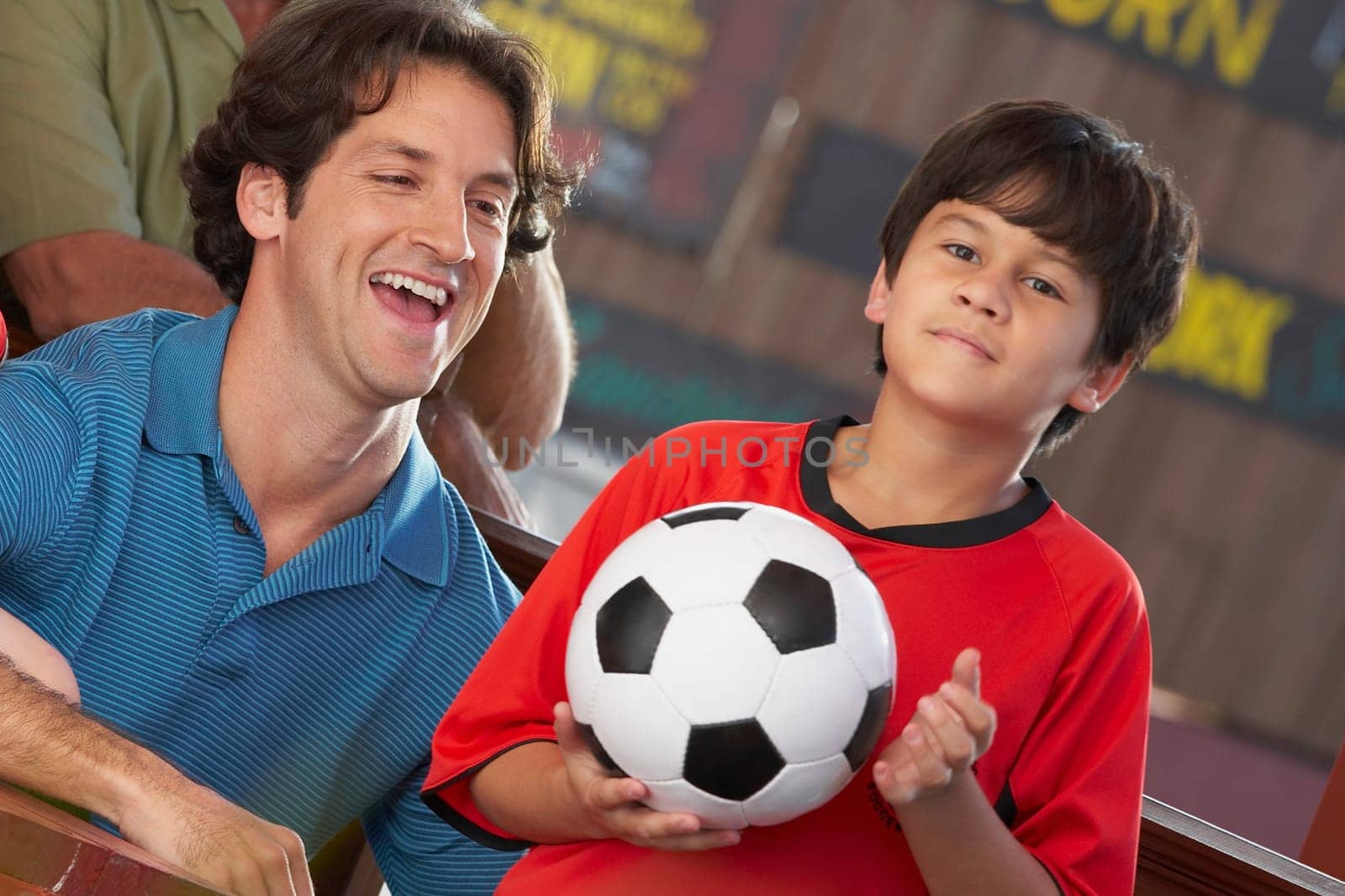 Portrait of a boy holding a soccer all with his father laughing beside him