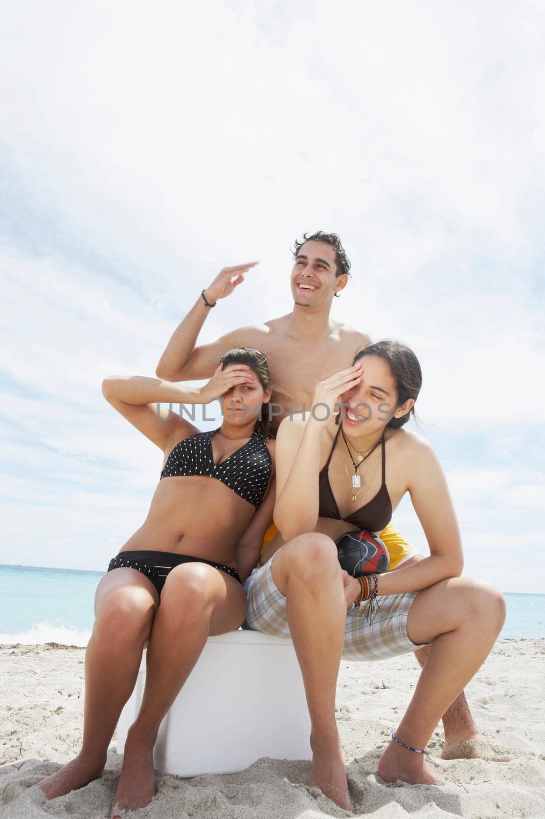 Portrait of two young women sitting on an ice box with a young man standing behind them