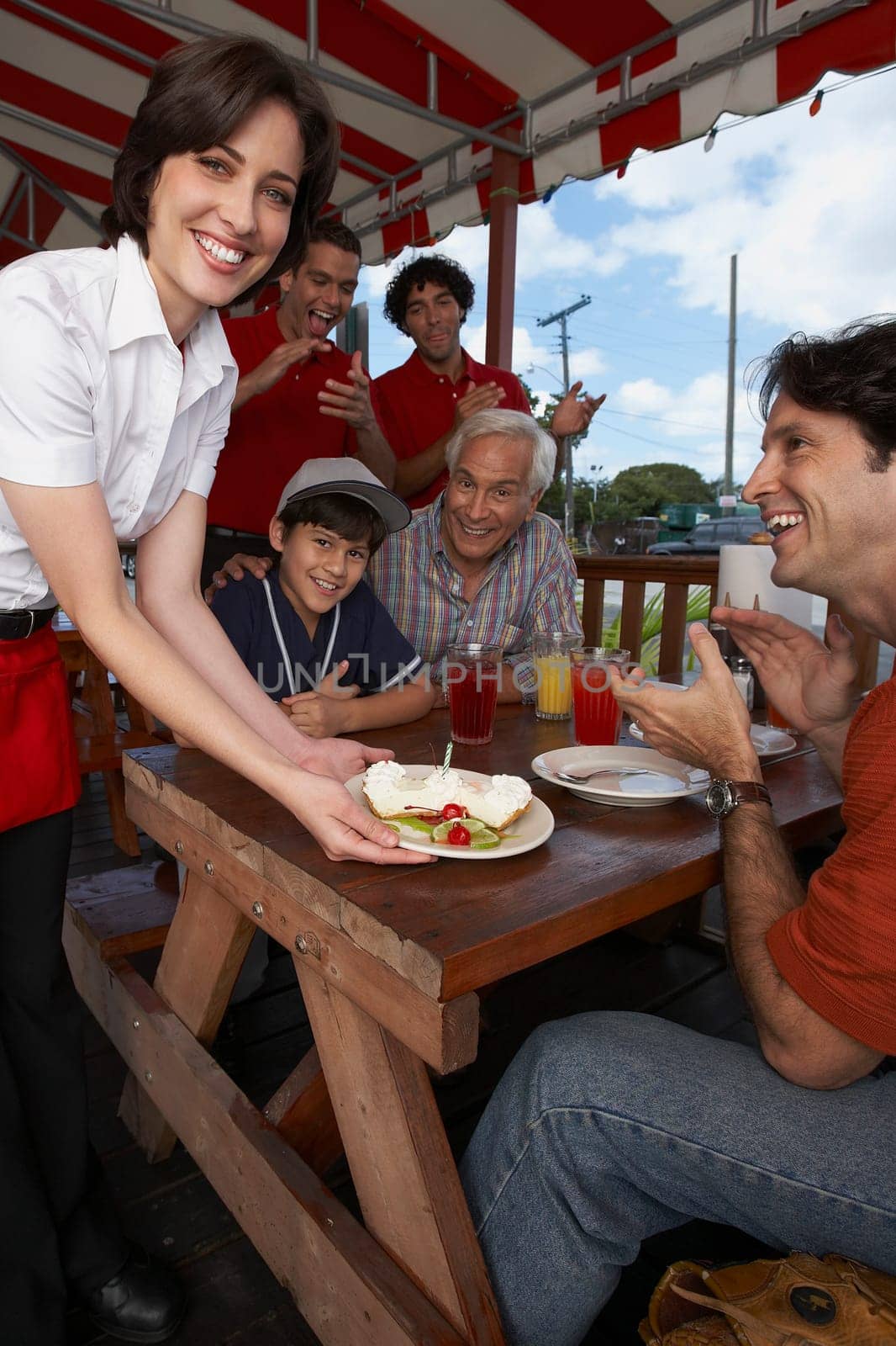 Portrait of a young woman serving dessert to a mid adult man celebrating his son's birthday in a restaurant