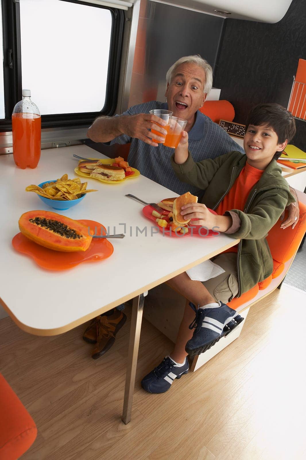 Portrait of a boy with his grandfather toasting glasses of juice at the dining table