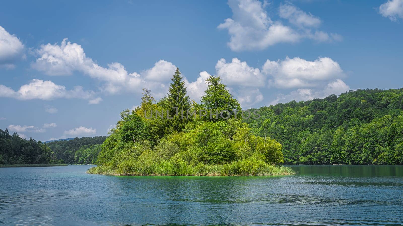 Small island on clean lake surrounded by hills and green lush forest, Plitvice Lakes National Park UNESCO World Heritage in Croatia