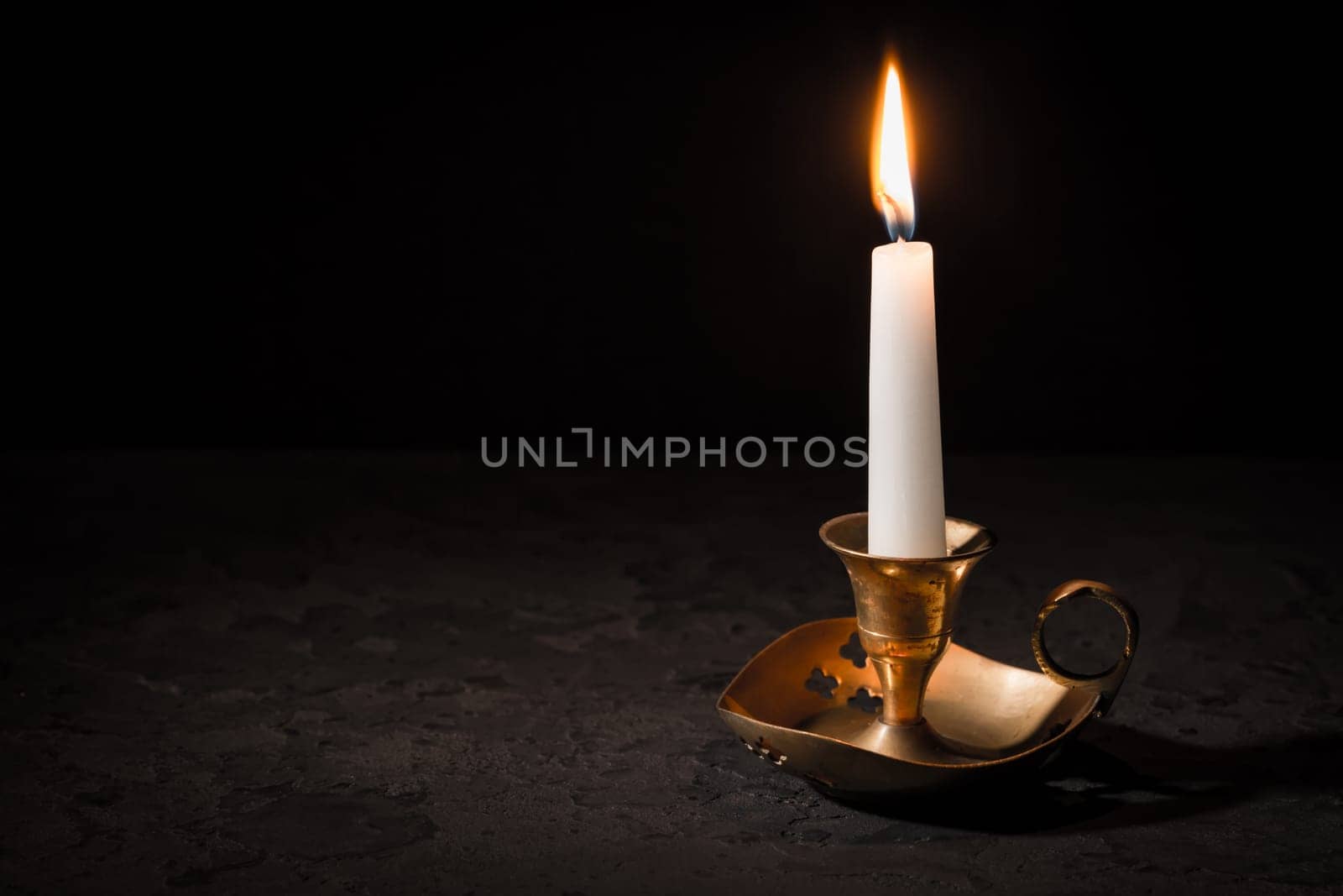 Burning candle in vintage candlestick on black background. Copy space for your text.