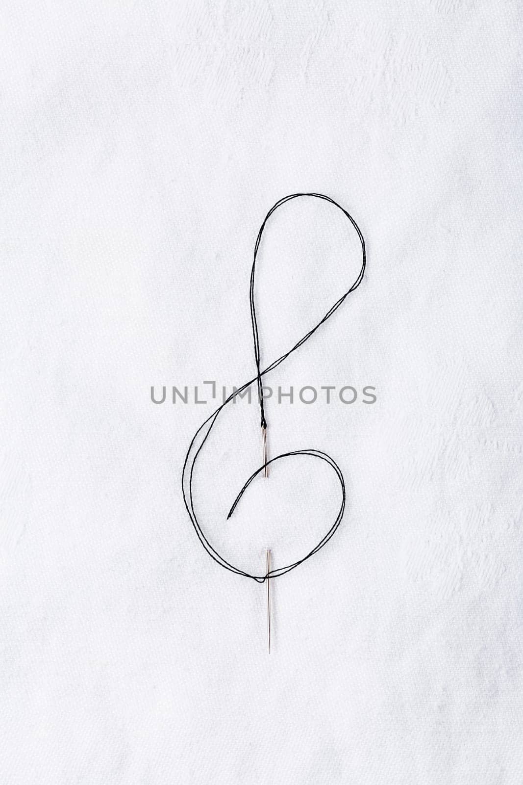 Macro of sewing needle in white fabric in violin key shape. Concept of handcraft and art.