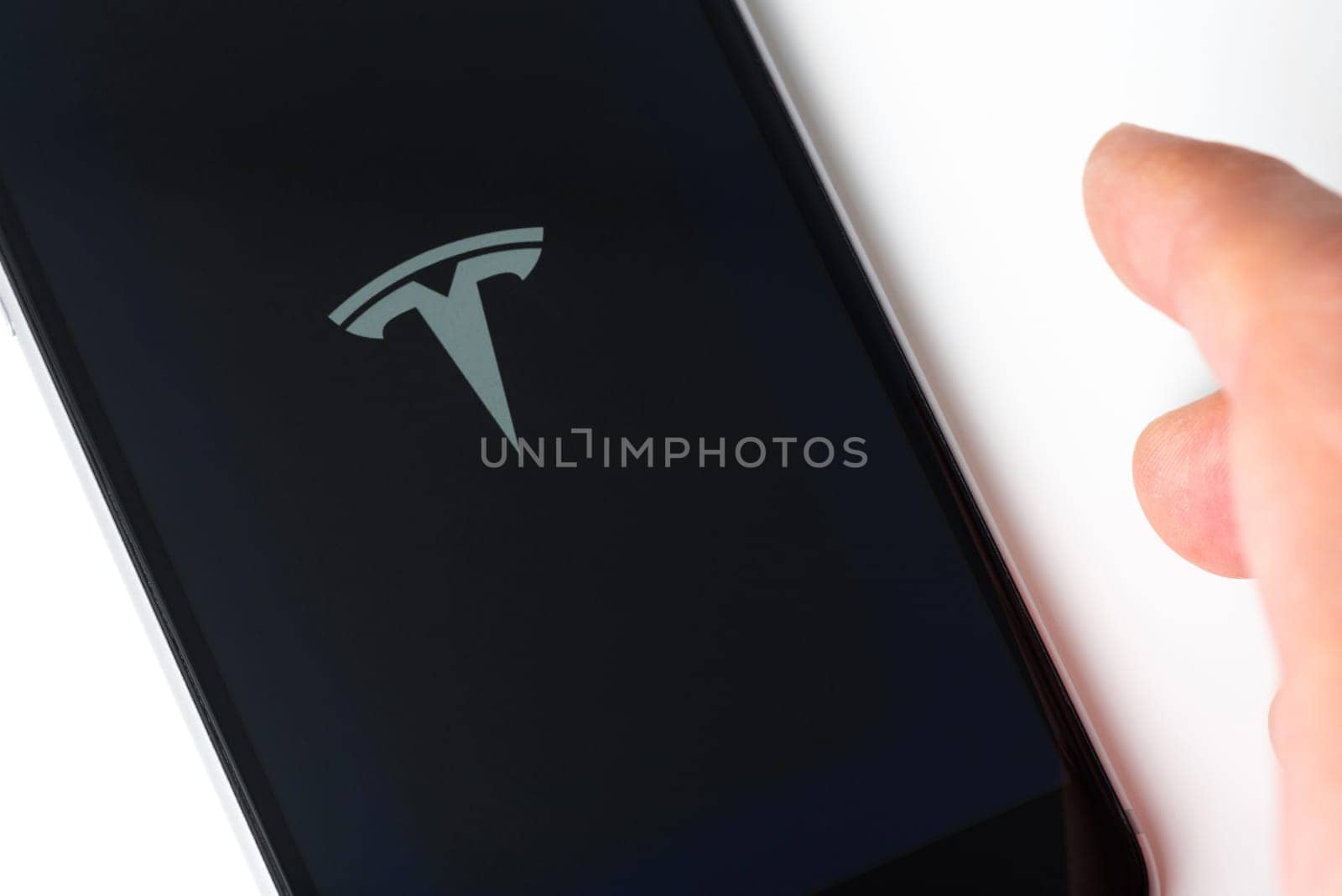 BAYONNE, FRANCE - CIRCA JANUARY 2021: Tesla app opening on Apple iPhone screen. The app is used to control and remotely monitor Tesla products. Hand about to grab phone.