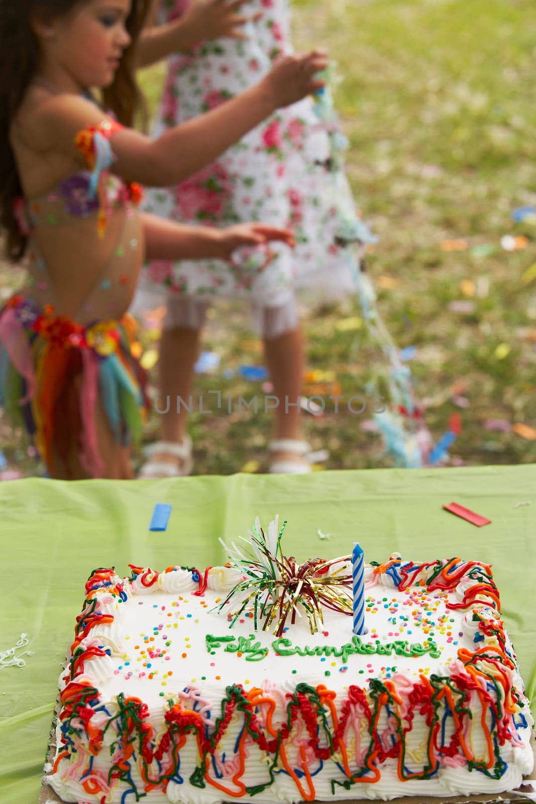 Birthday cake on a table at a birthday party with two children in the background