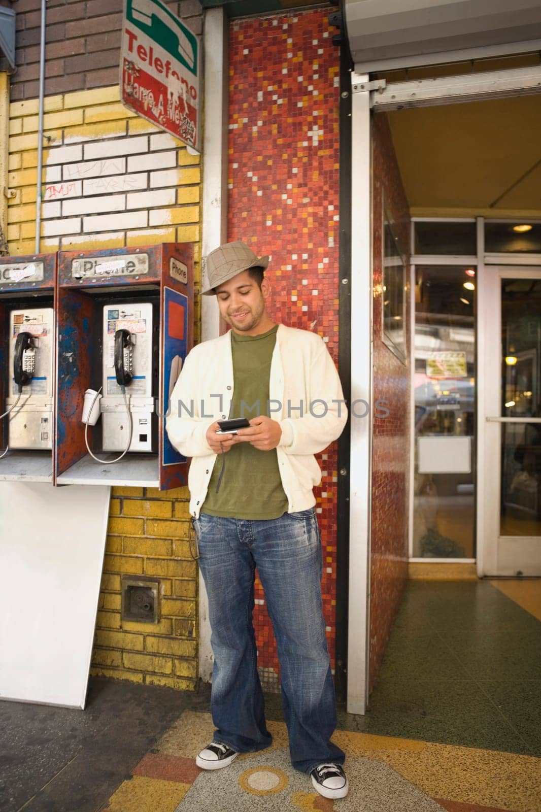 Young man using a mobile phone near a pay phone