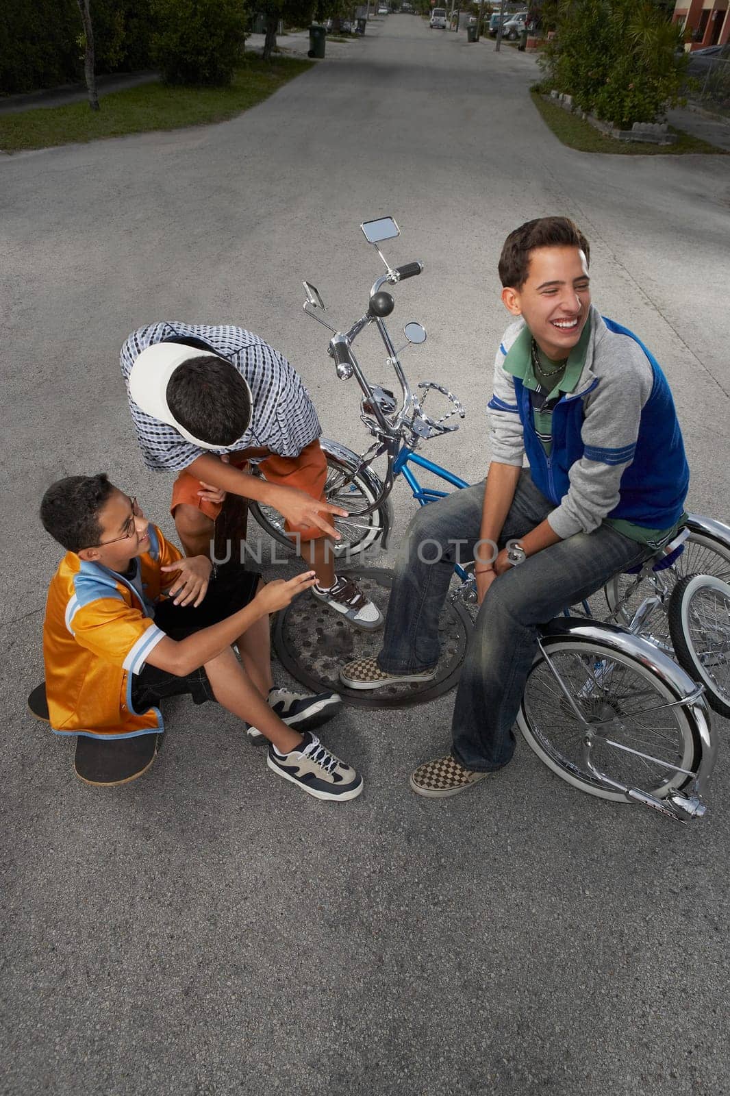 High angle view of a teenage boy and a boy gesturing at their friend sitting on a low rider bicycle